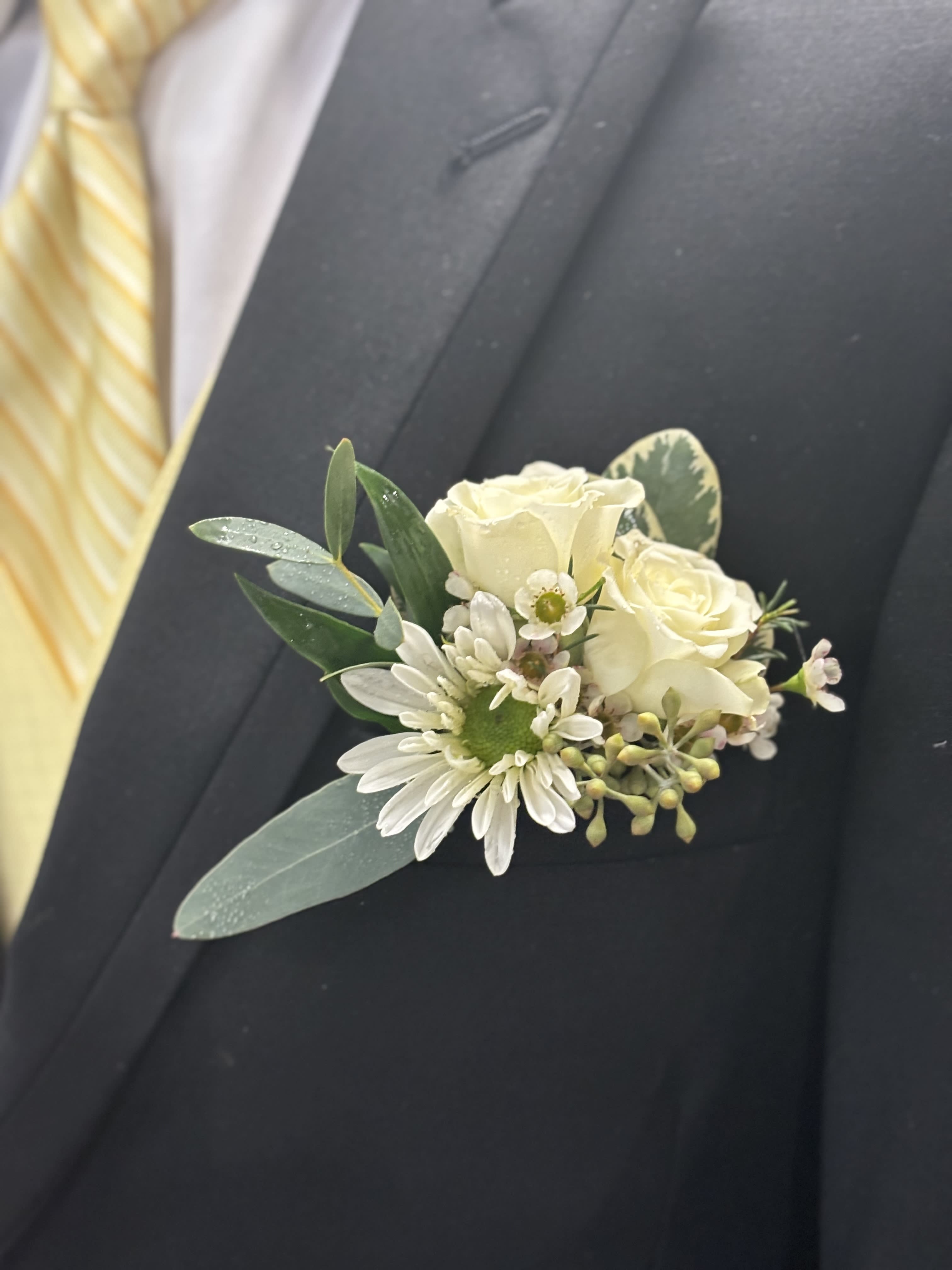 White boutonniere with roses and daisies on a dark suit lapel