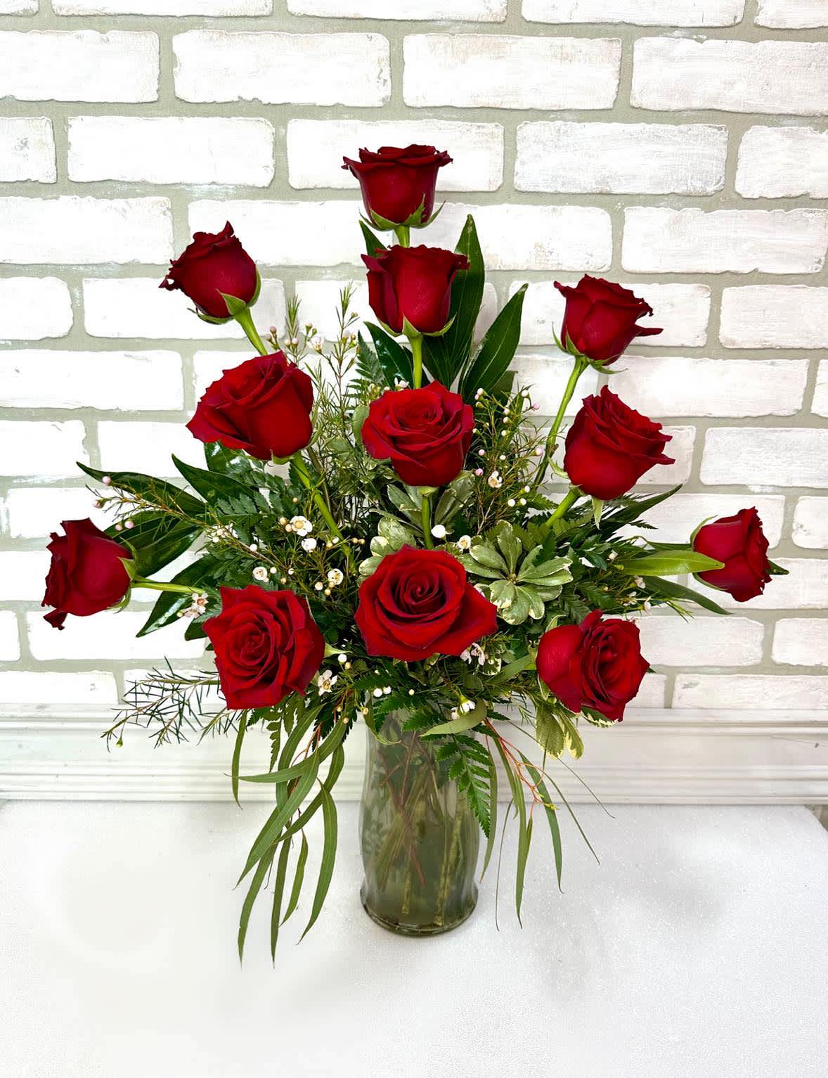 Red roses arranged in a clear glass vase with greenery