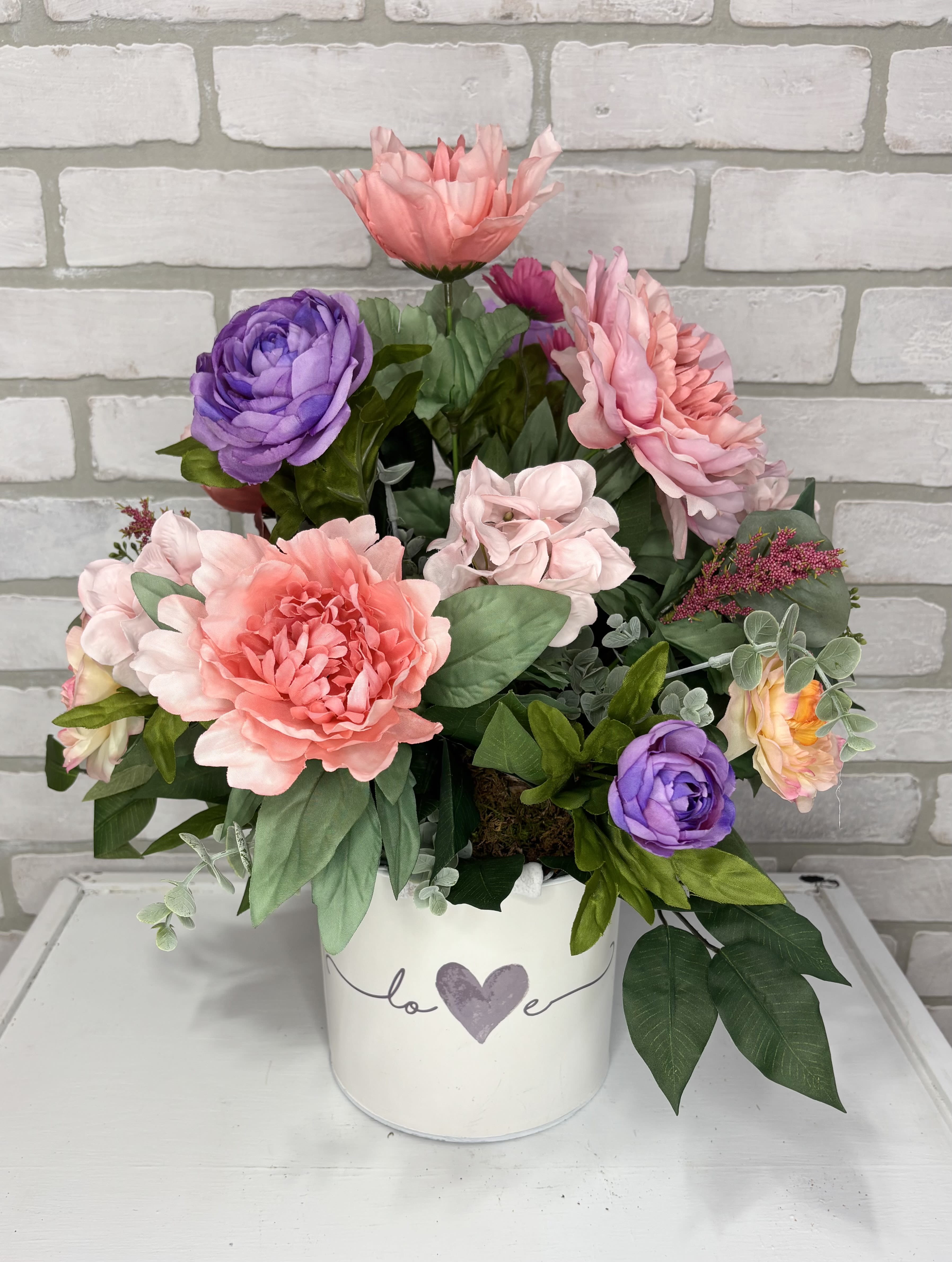 Pink and purple flowers arranged in a white heart-decorated container