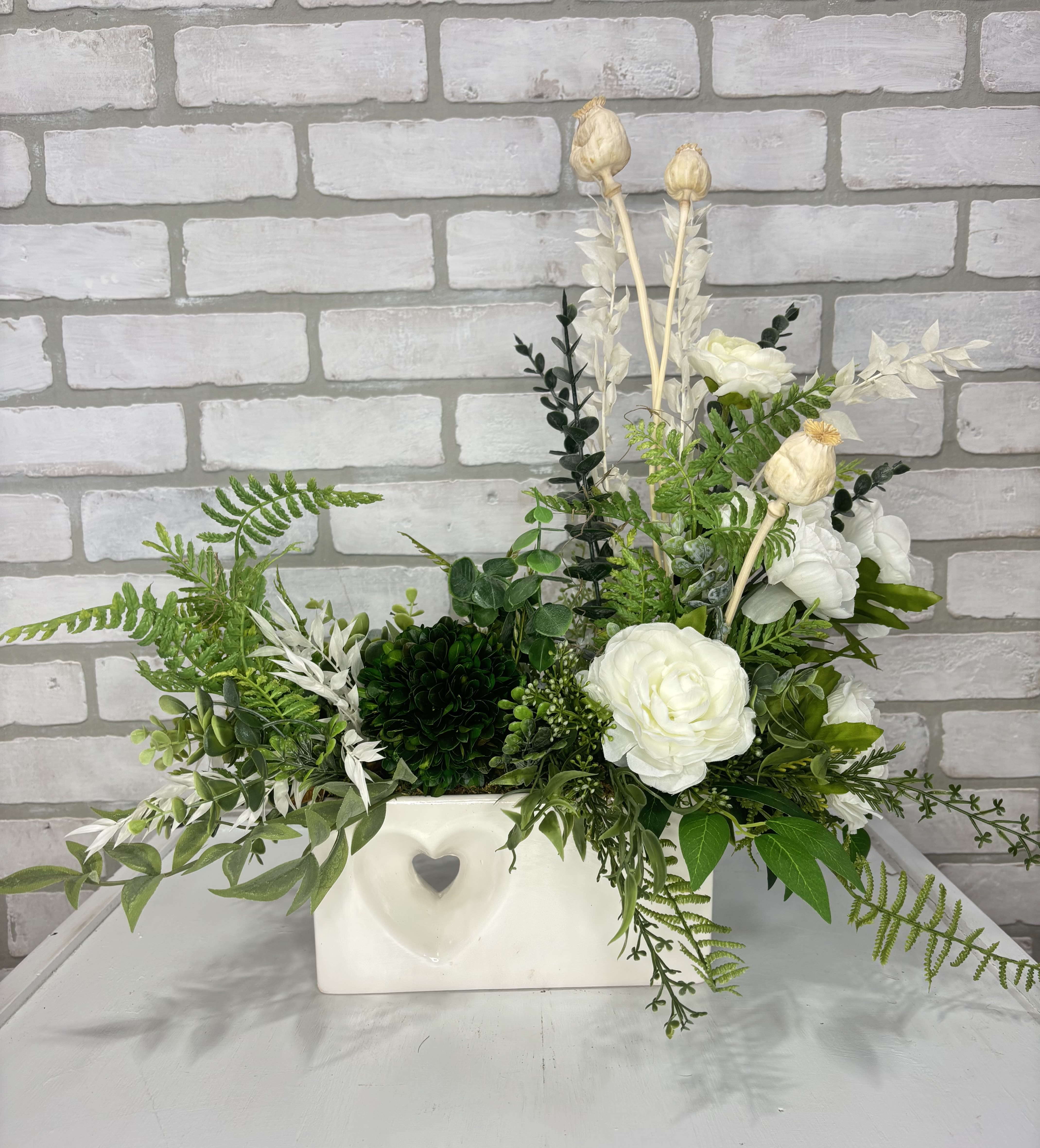 White floral arrangement in a rectangular vase with mixed greenery