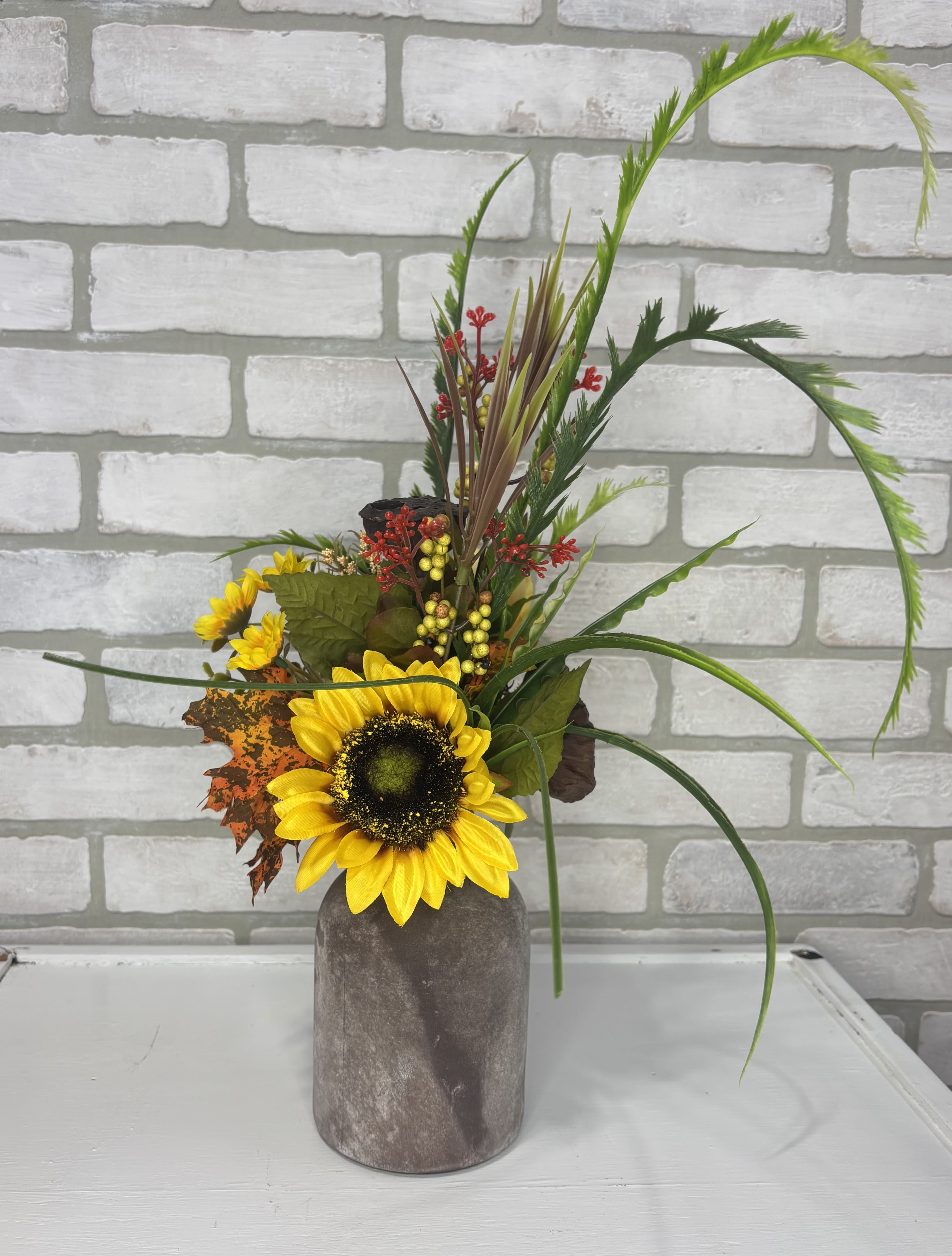 Sunflower arrangement in a gray vase with autumn foliage and berries