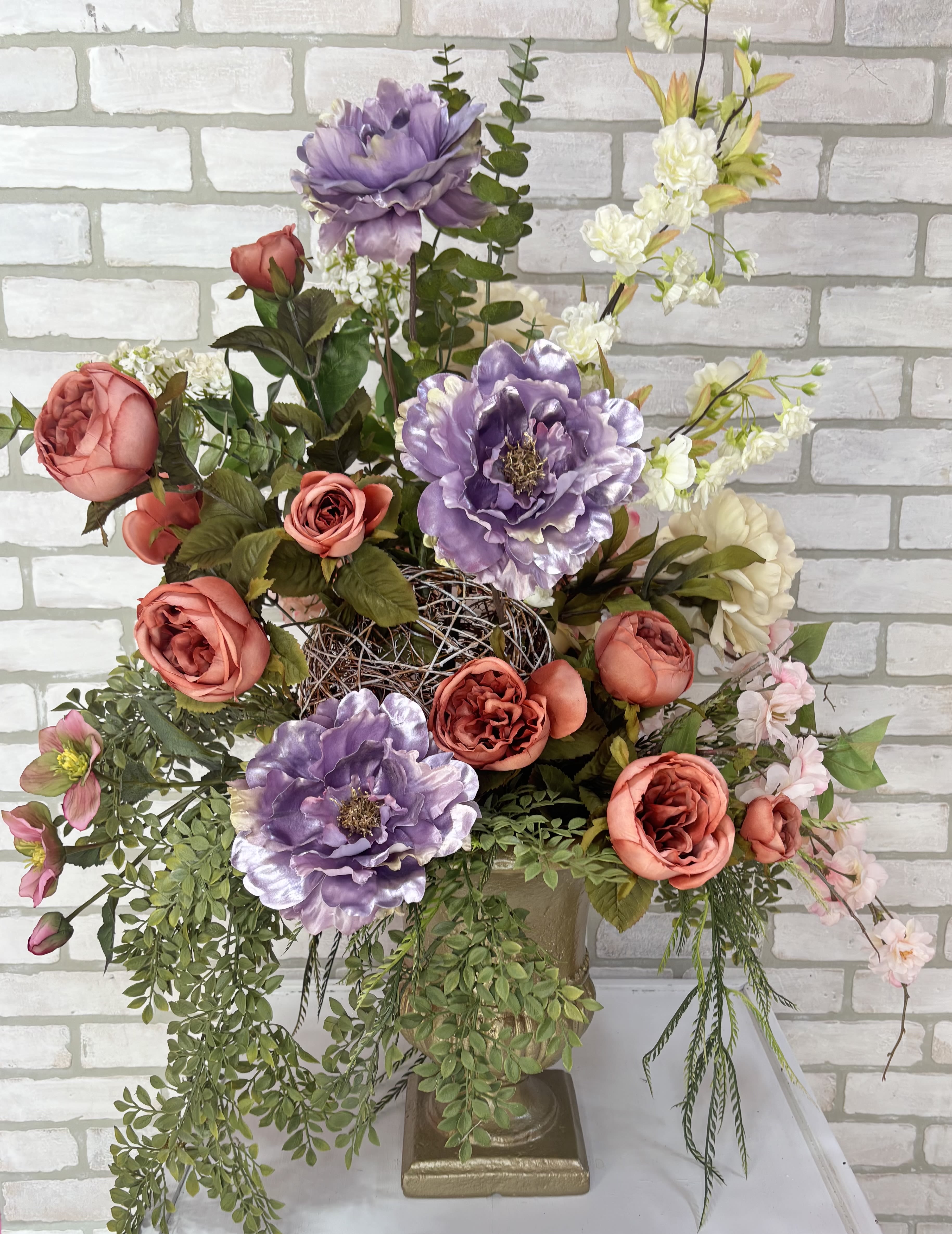 Large floral arrangement with coral and lavender blooms in a gold vase