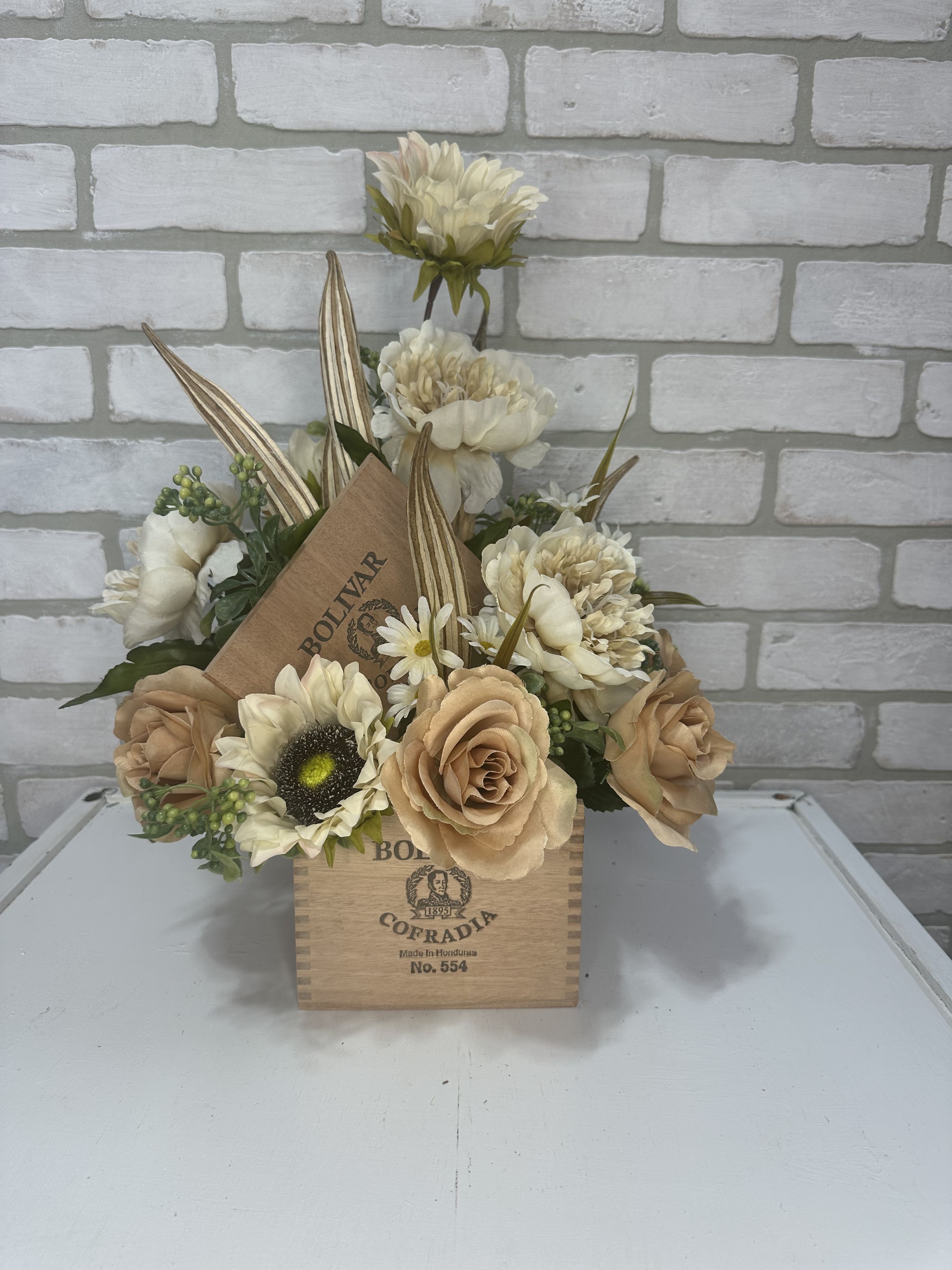 Cream and tan floral arrangement in a wooden cigar box
