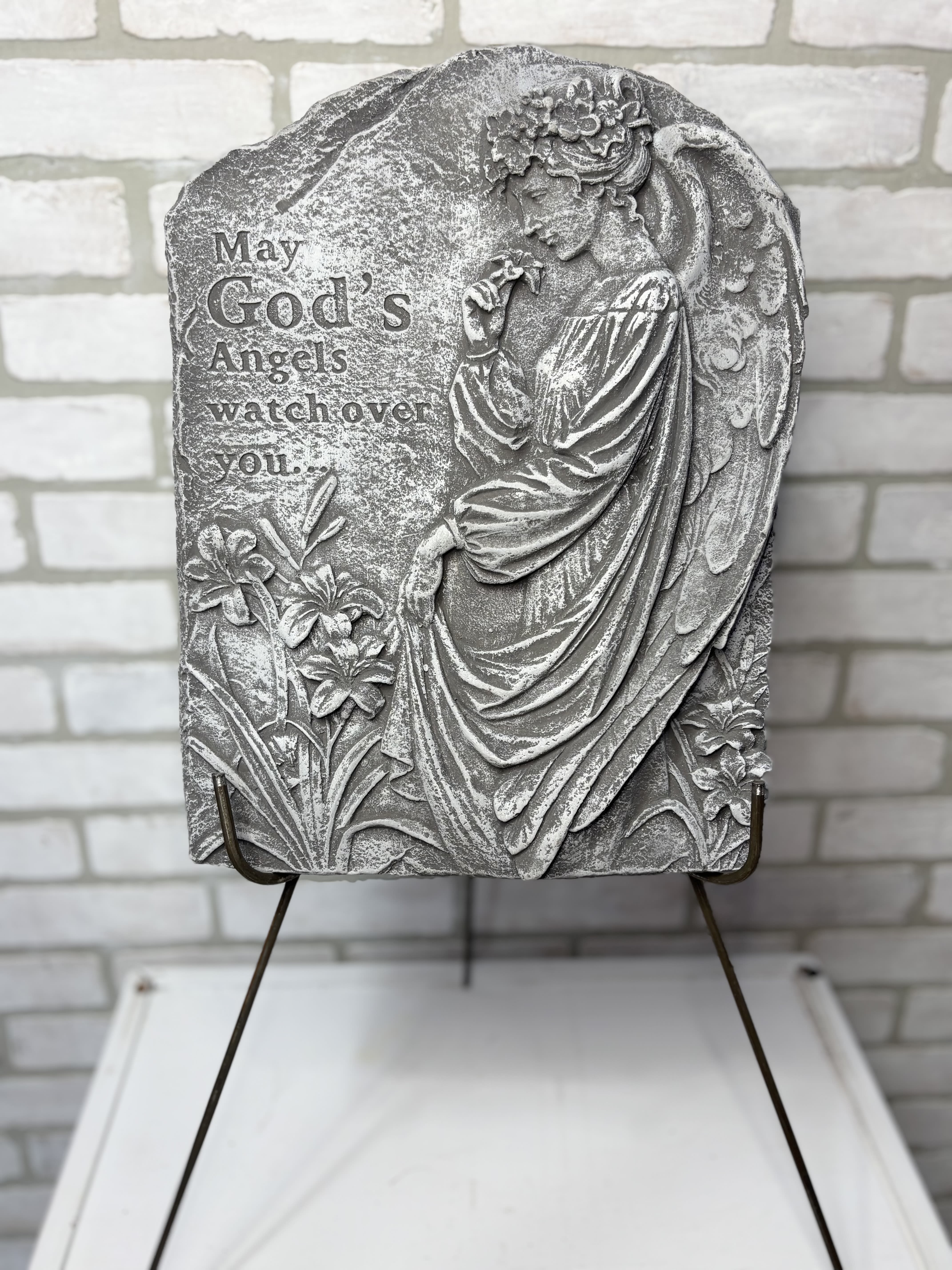 Gray memorial plaque with an angel and flowers on a stand