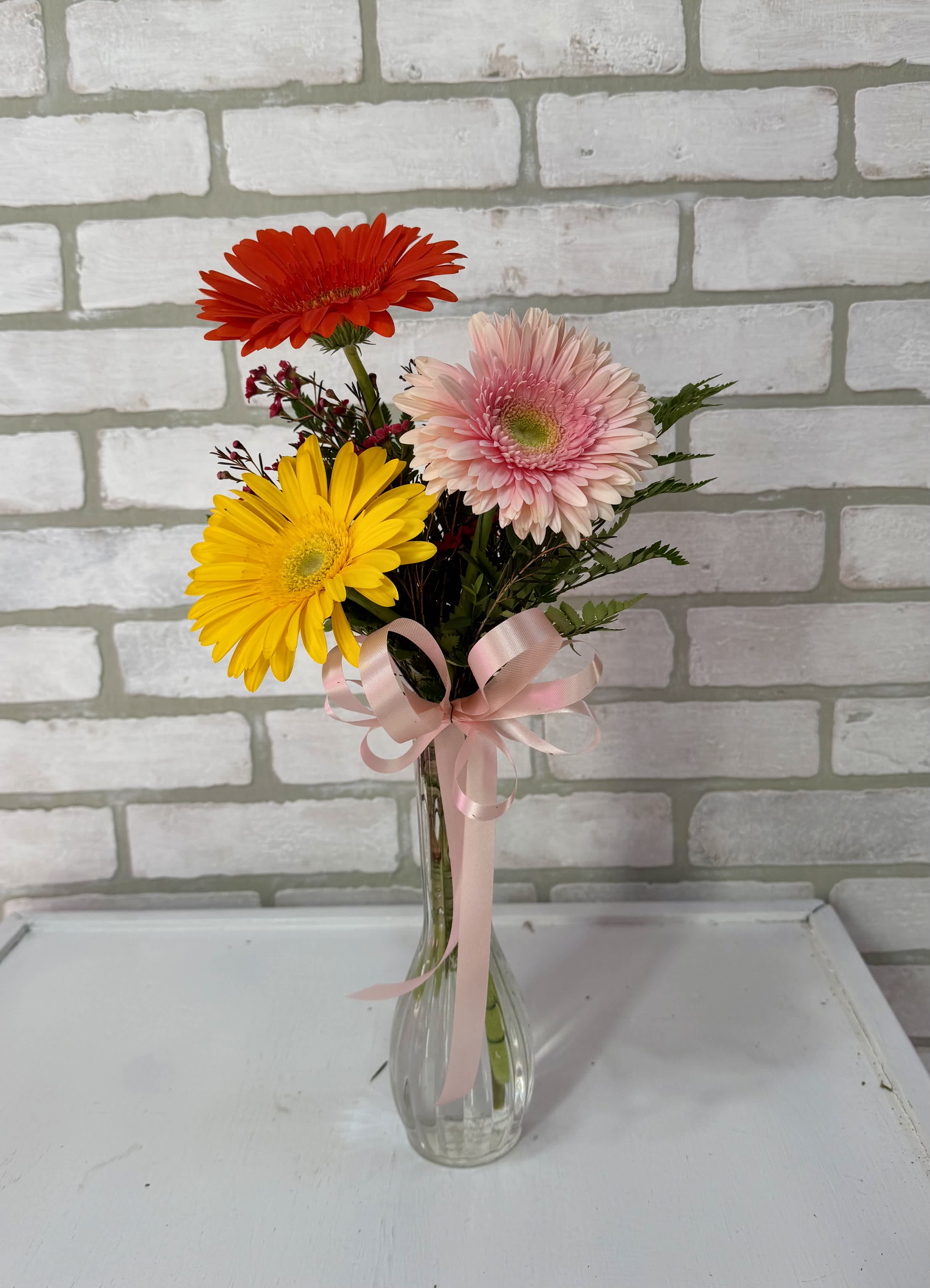 Gerbera daisies in a clear glass vase with a pink ribbon