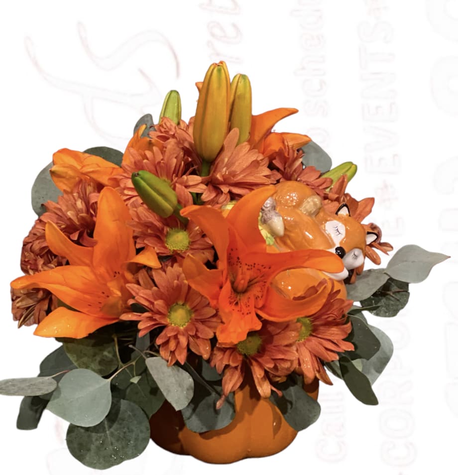 Orange lilies and mums arranged in a pumpkin-shaped container with a fox accent