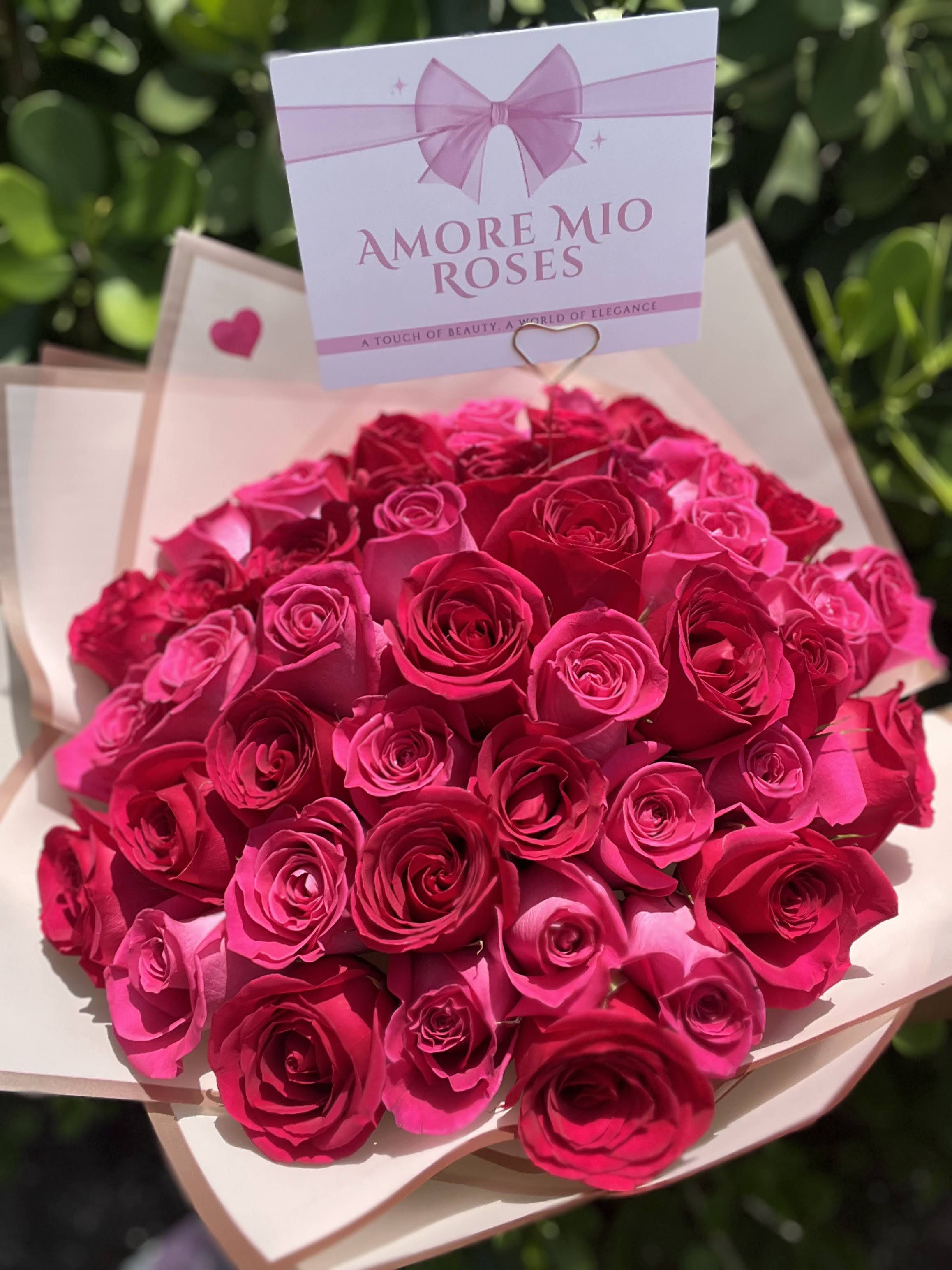 Bouquet of bright pink roses wrapped in pale paper with a gift card