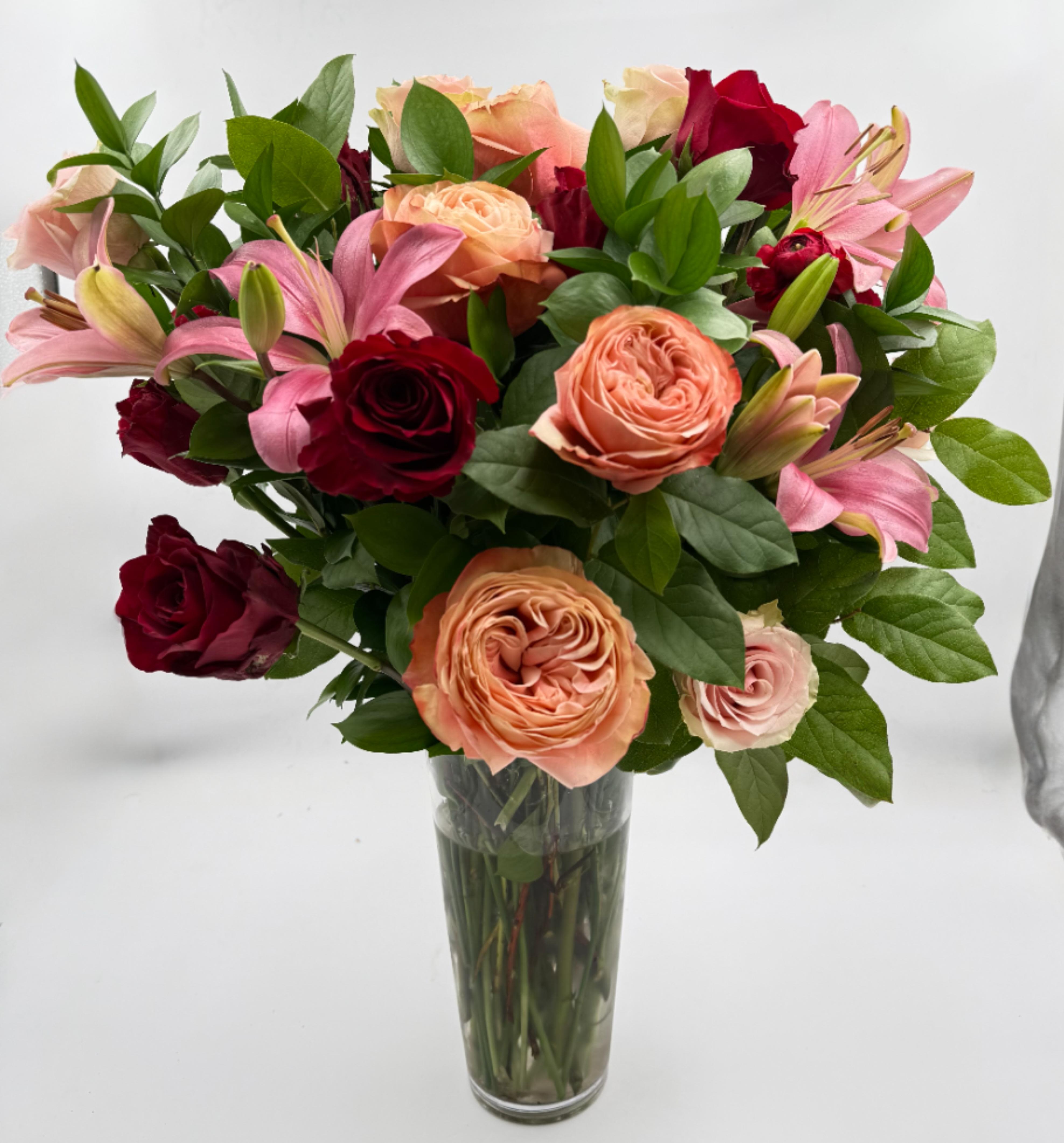 Bouquet of pink, peach, and red roses with lilies in a clear glass vase