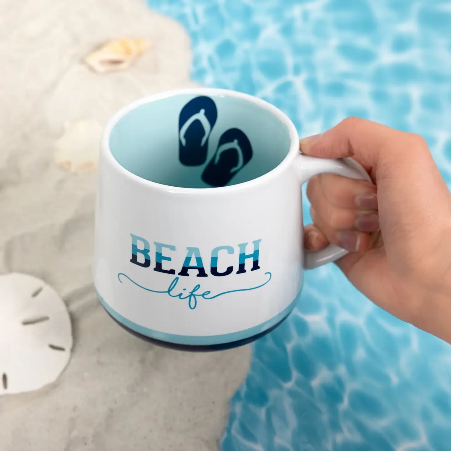 Beach Life - 18 oz Mug - This 18 oz stoneware mug has beaker-shaped walls and a glossy finish. It features a handle with rounded edges for a comfortable and sturdy grip. The coffee cup features a triple-tone white, teal blue, and dark blue striped pattern and a "Beach Life" tri-colored blue sentiment on both sides of the mug. Additionally, the interior is blue, with a large pair of flip-flops on the side wall. Microwave &amp; dishwasher safe. They are packaged securely in a die-cut box for safe shipping. The beach is a beautiful getaway to soak up the sun, ride the boat, sit next to the fire, stick your toes in the sand by the coastal ocean, and create summertime memories that will last a lifetime. So give your beach lover friend the best drinkware mug to add to their collection.