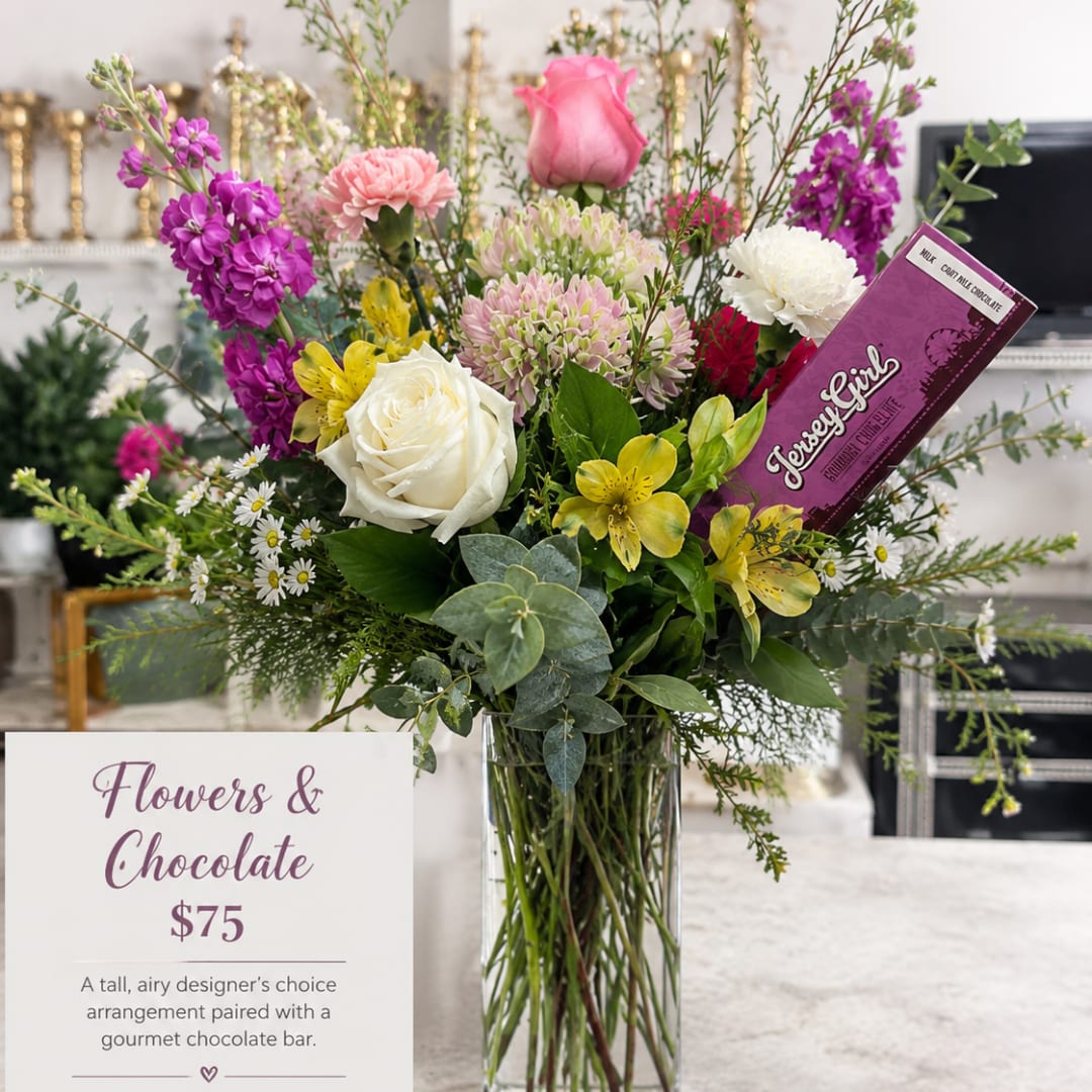 Tall mixed bouquet in a glass vase with a chocolate bar tucked in.