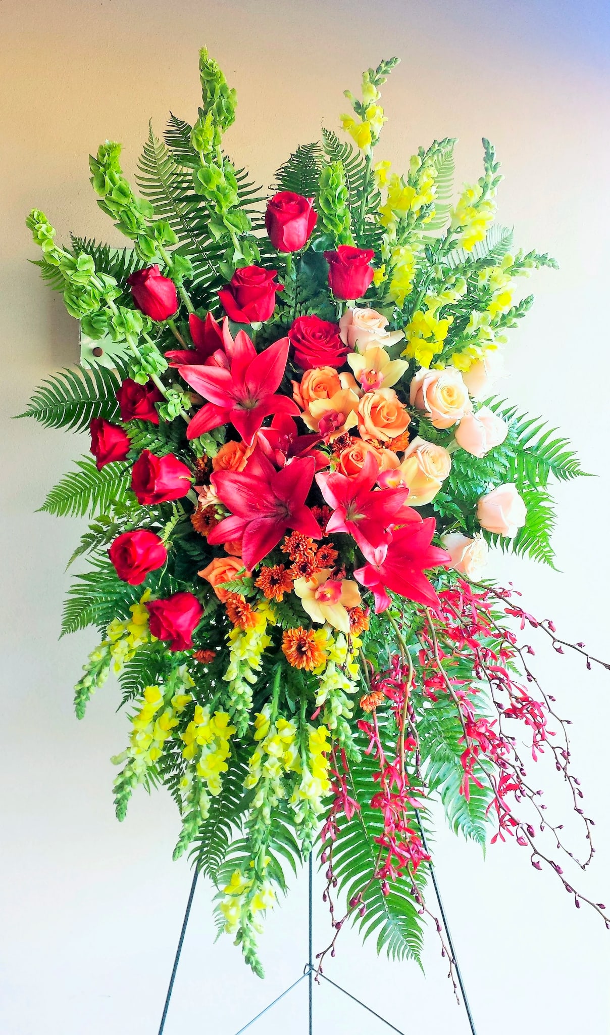 Large standing floral spray with red roses, lilies, and yellow blooms