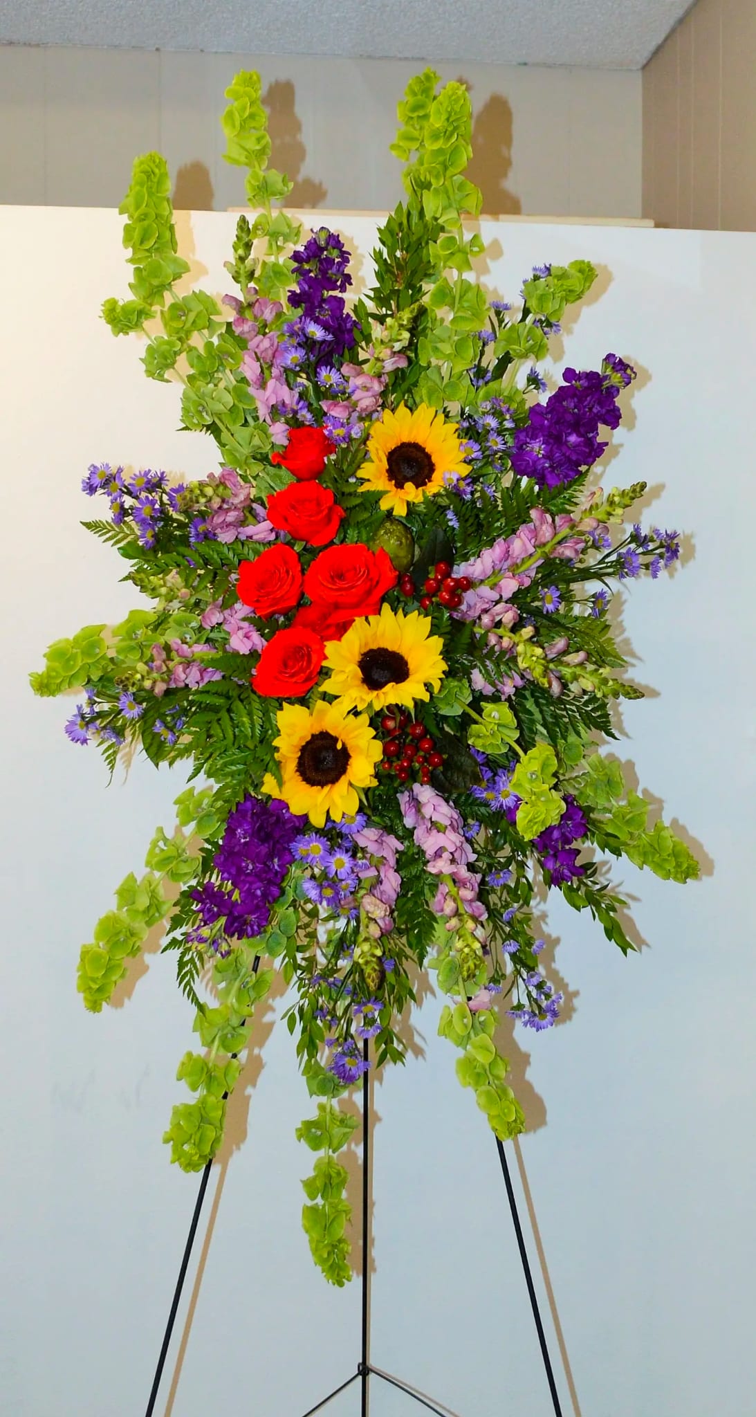 Tall standing floral spray with sunflowers, red roses, and purple blooms