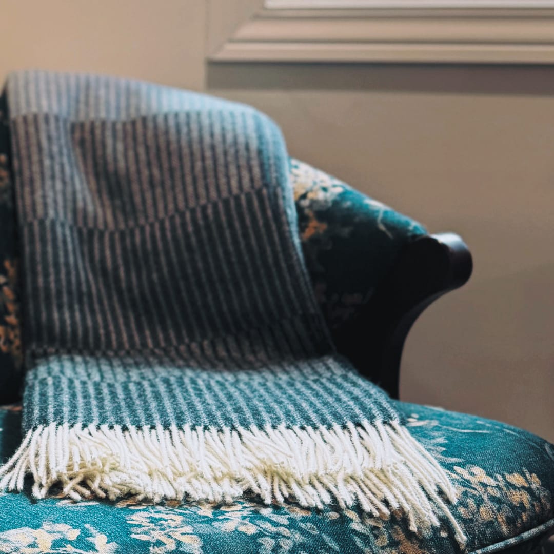 A striped woven blanket draped over a teal floral armchair