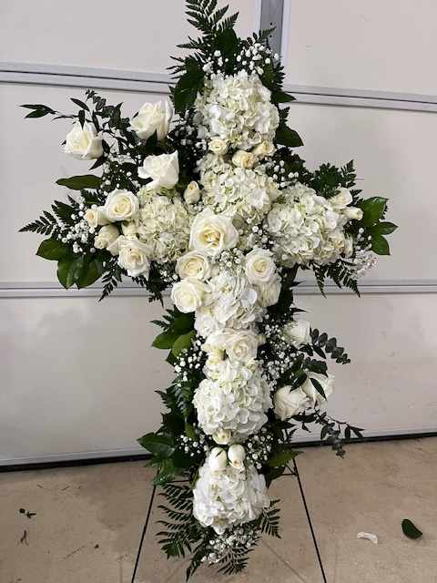 White floral cross arrangement with roses and hydrangeas on a stand