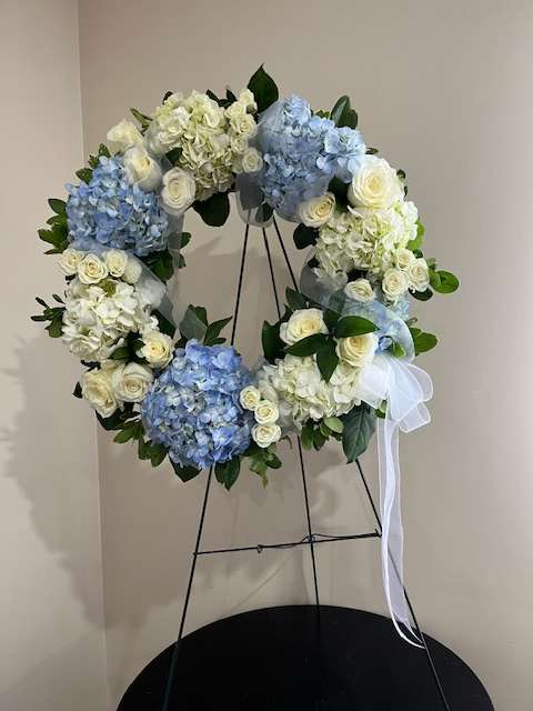 Blue and white floral wreath on a stand with a white ribbon