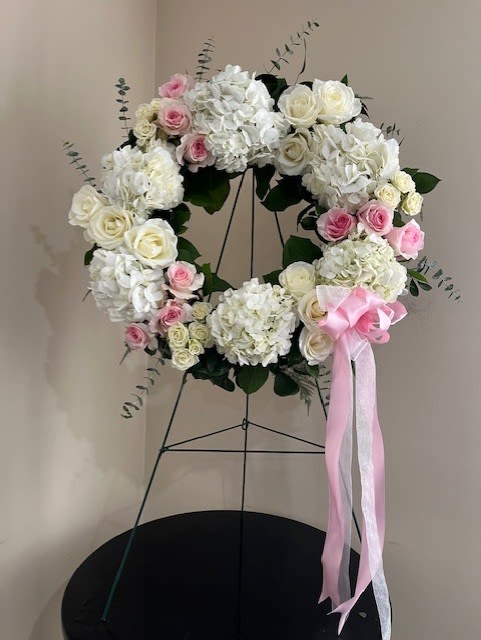 White and pink floral wreath on a stand with a pink ribbon