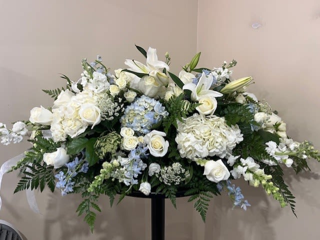 Large white floral arrangement with lilies, roses, and hydrangeas on a stand