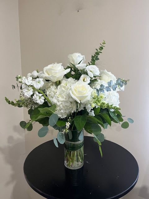 White roses and hydrangeas with eucalyptus in a clear glass vase on a round black table