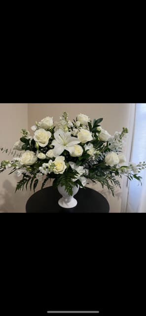 White roses and lilies arranged in a white urn vase