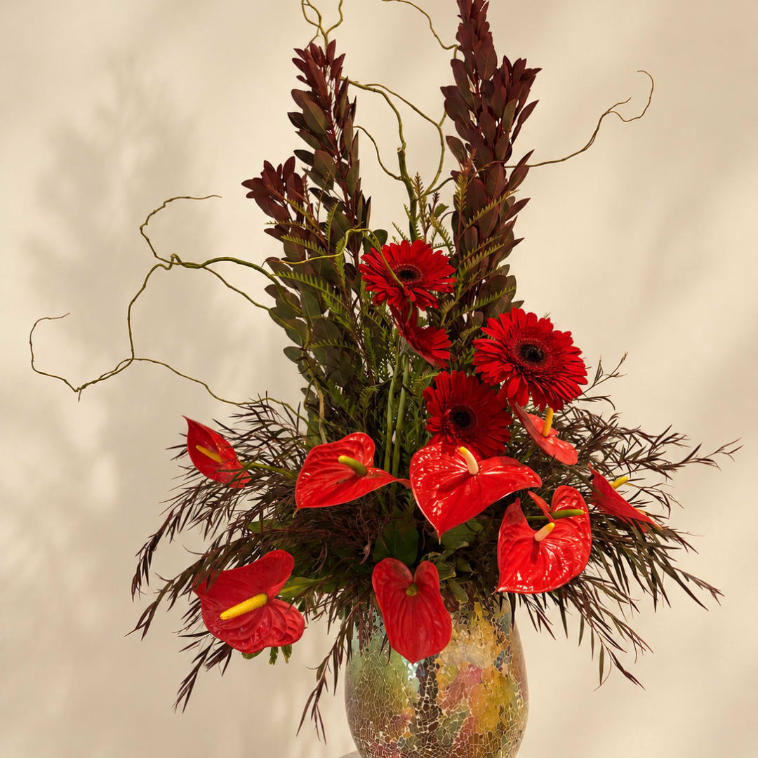 Red gerbera daisies and anthuriums in a glass vase