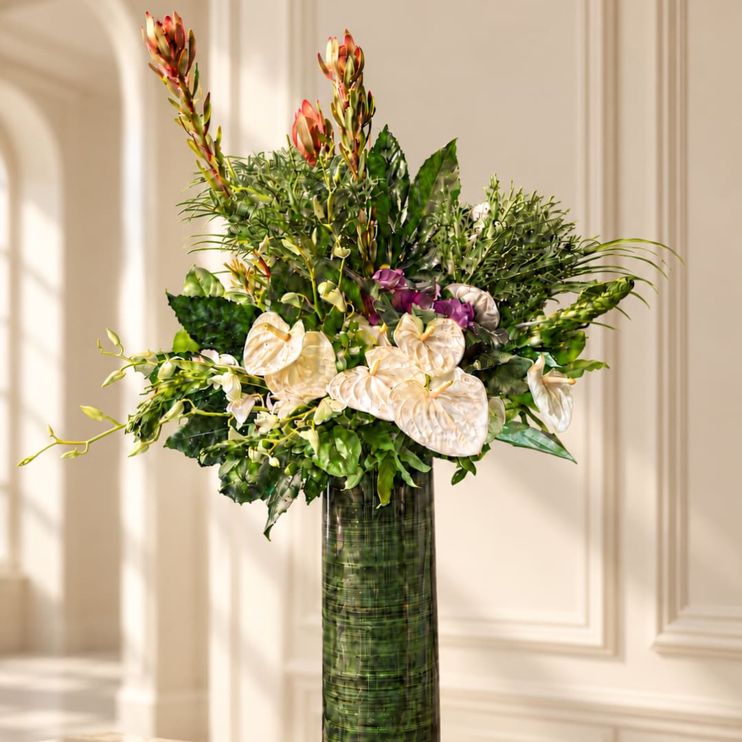 Tall arrangement of white anthuriums and mixed tropical flowers in a green vase