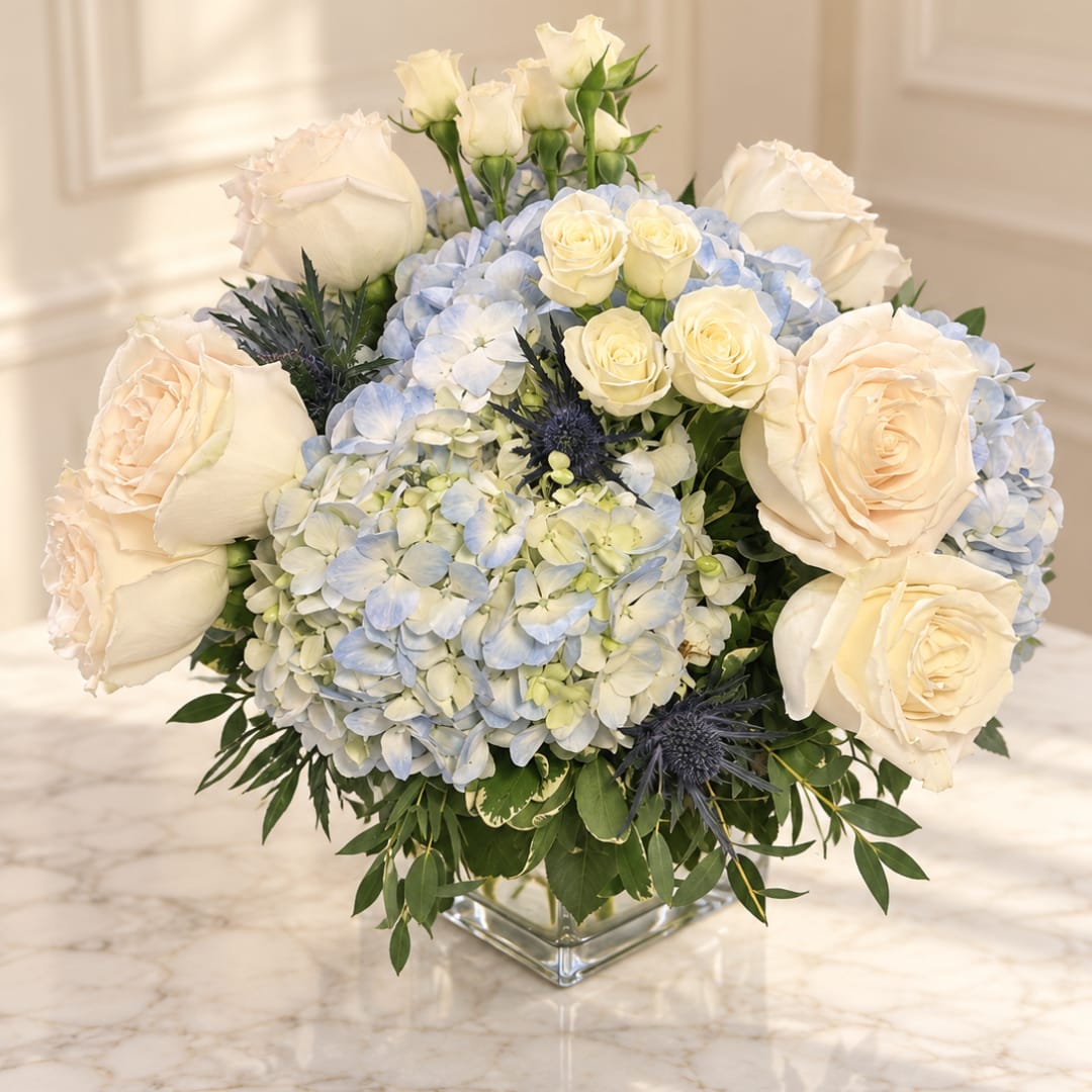 Cream roses and blue hydrangeas in a clear square vase