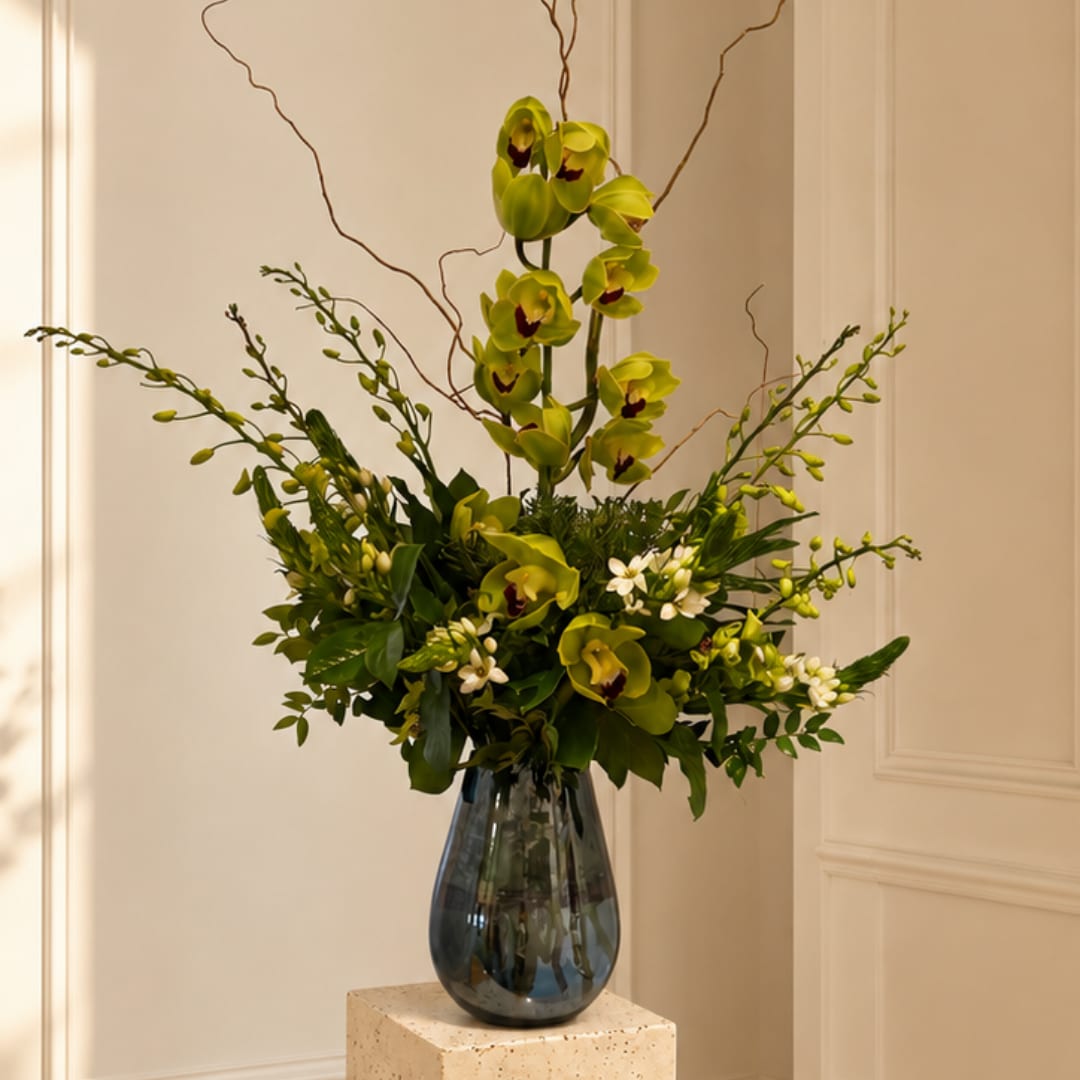 Green orchid arrangement in a dark glass vase