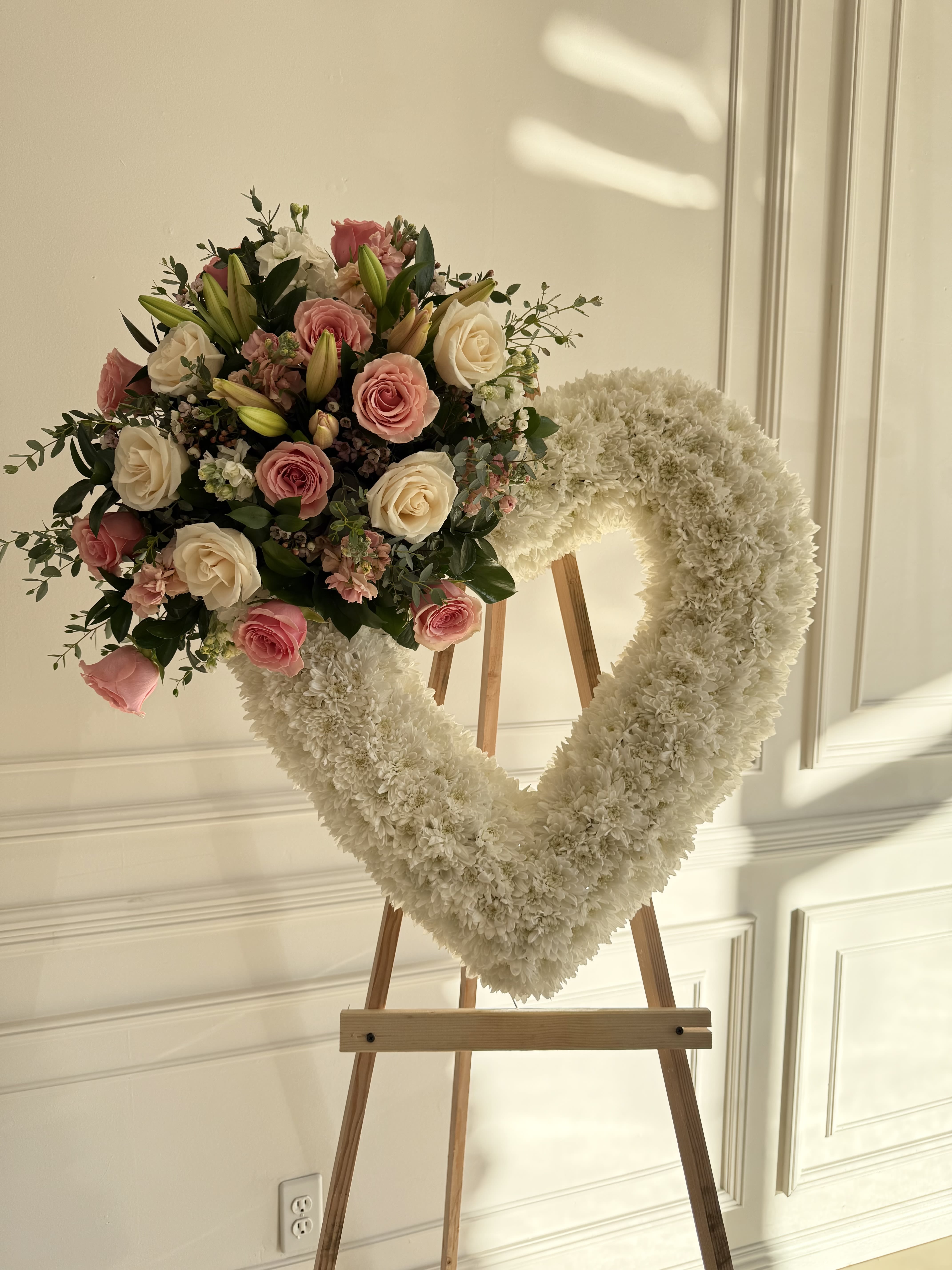 Heart-shaped white floral wreath with pink roses on a wooden easel