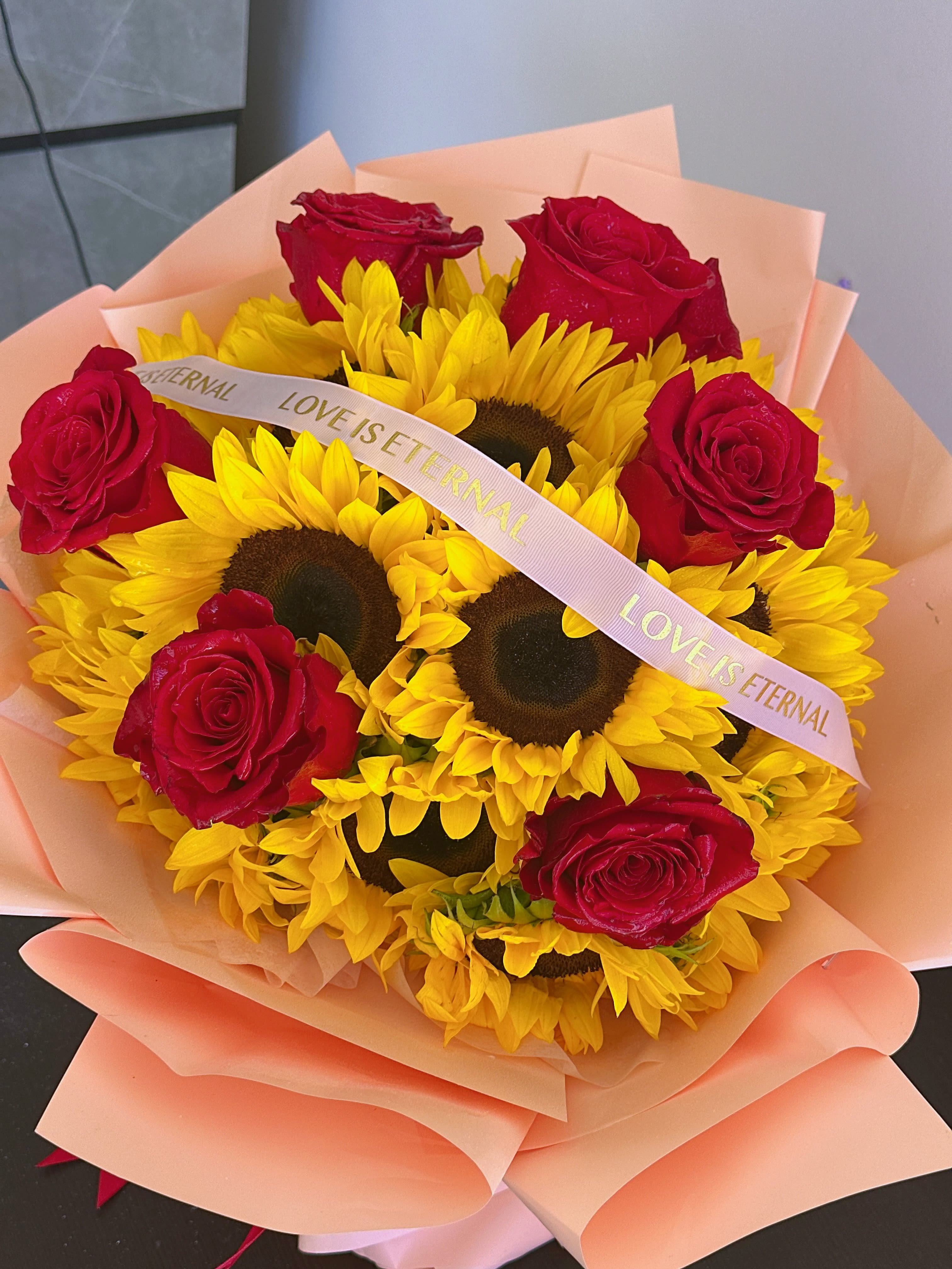 Bouquet of red roses and yellow sunflowers wrapped in peach paper
