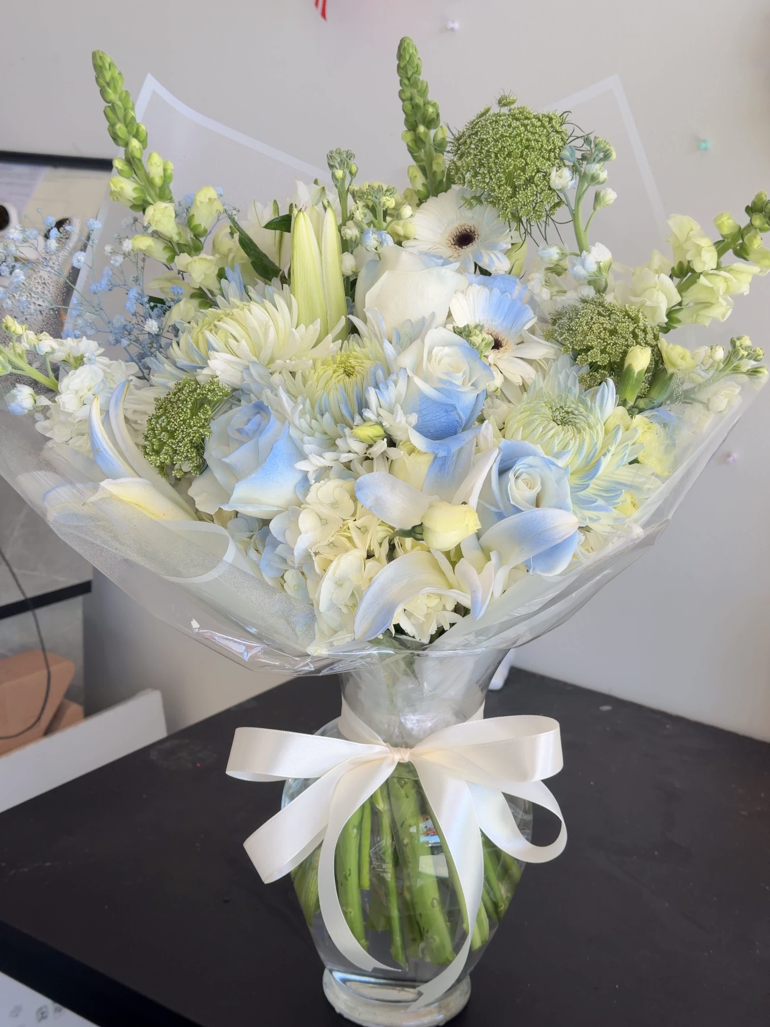 White and pale blue bouquet in a glass vase with a ribbon bow