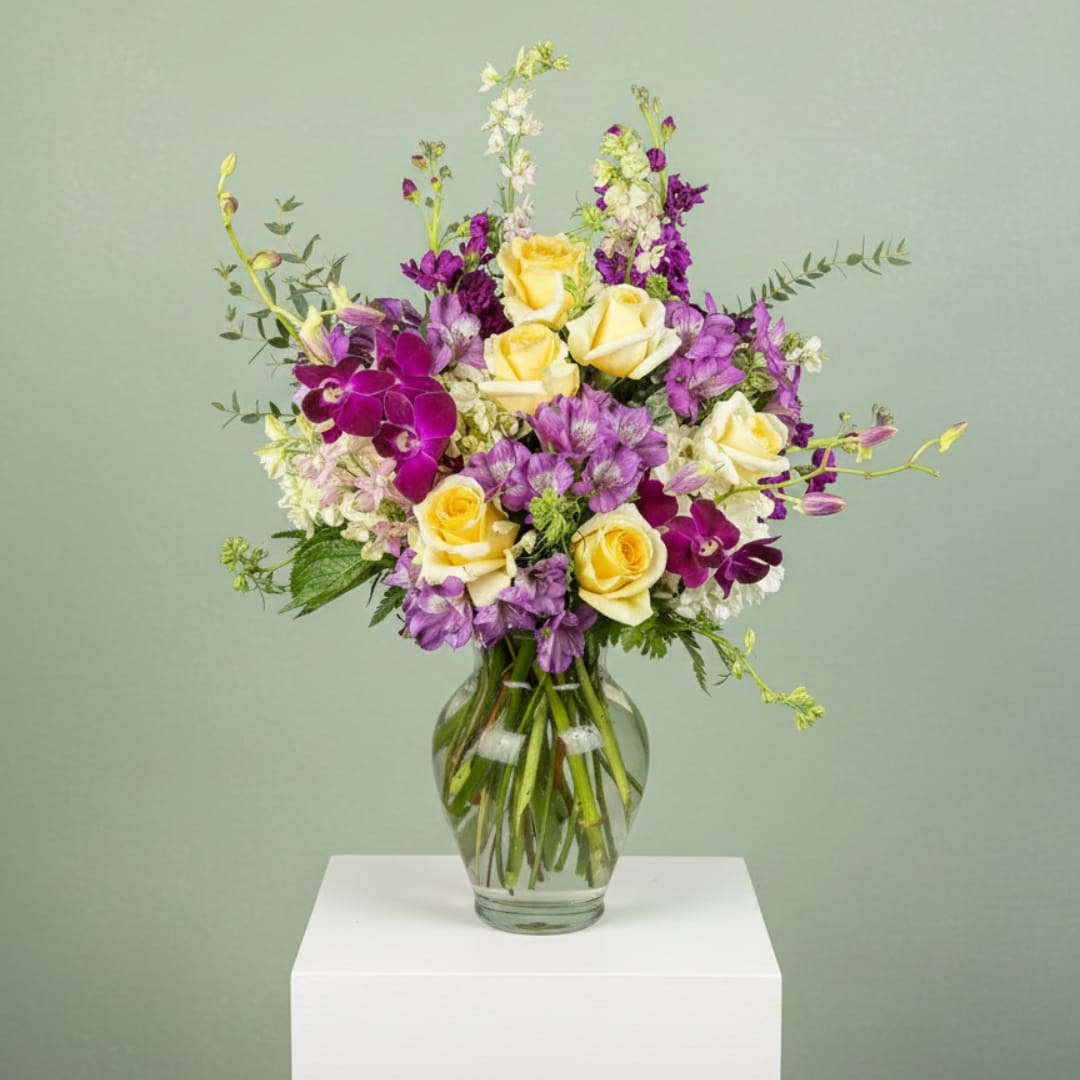 Yellow roses and purple orchids in a clear glass vase