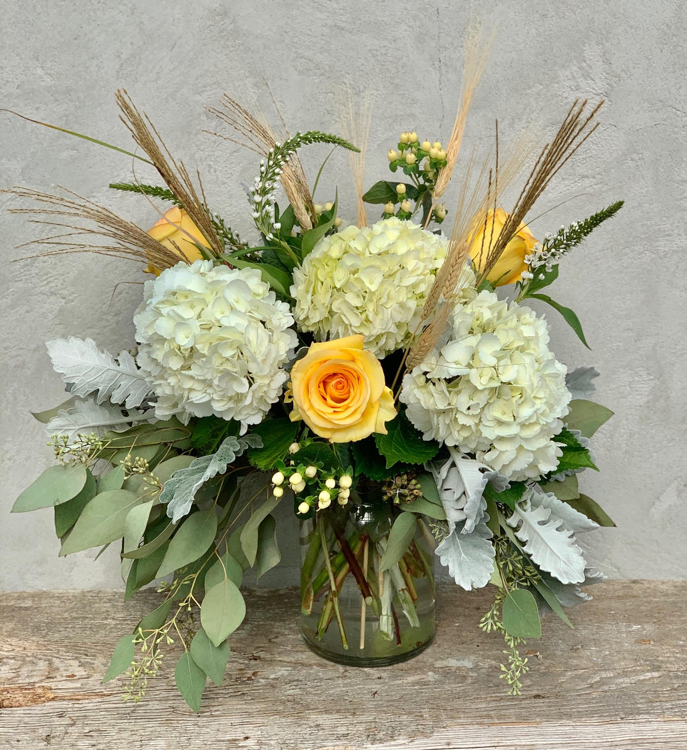 Yellow roses and white hydrangeas in a glass vase with dried grasses