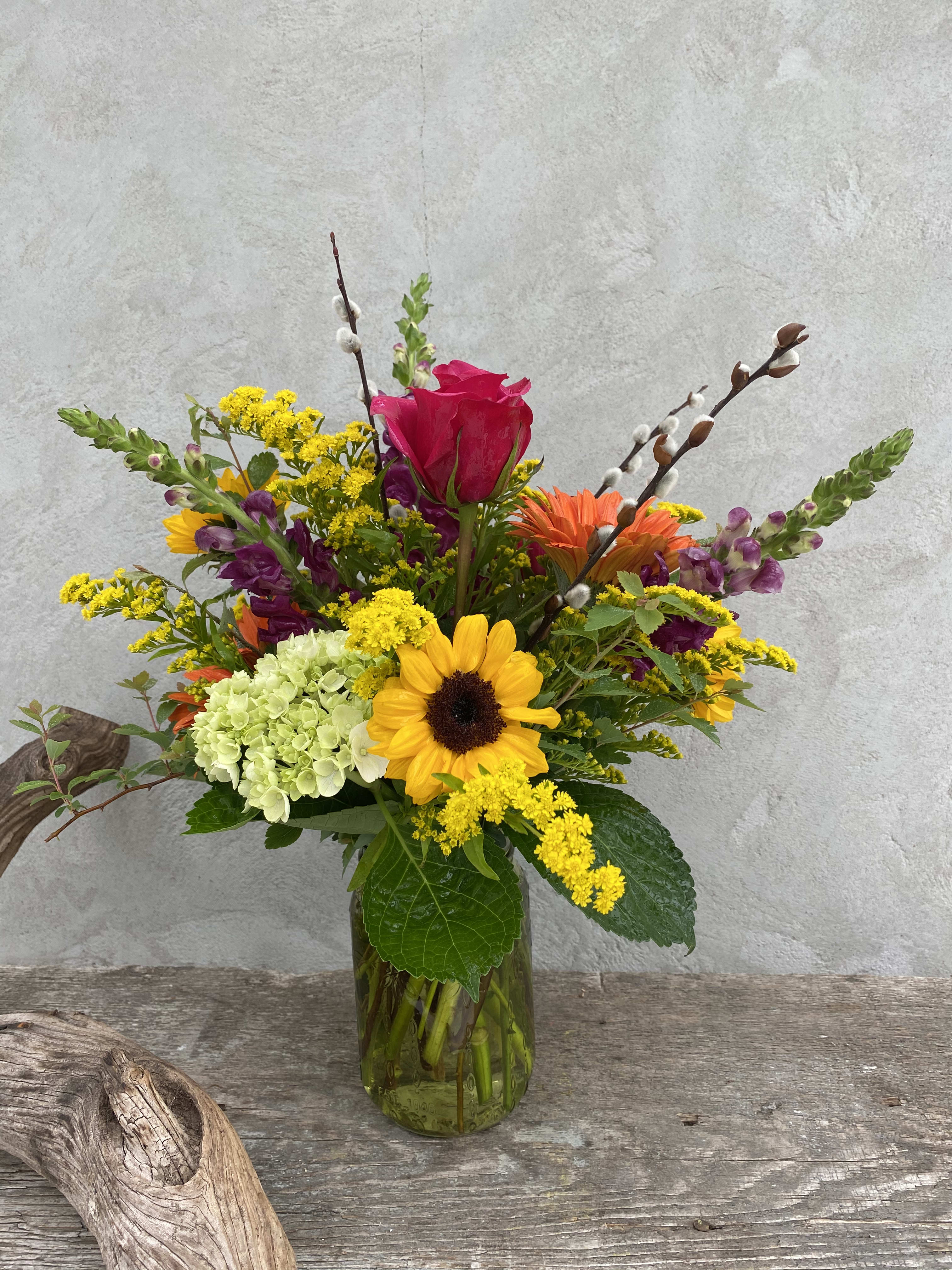 Colorful mixed flower arrangement in a glass vase with a sunflower and pink rose