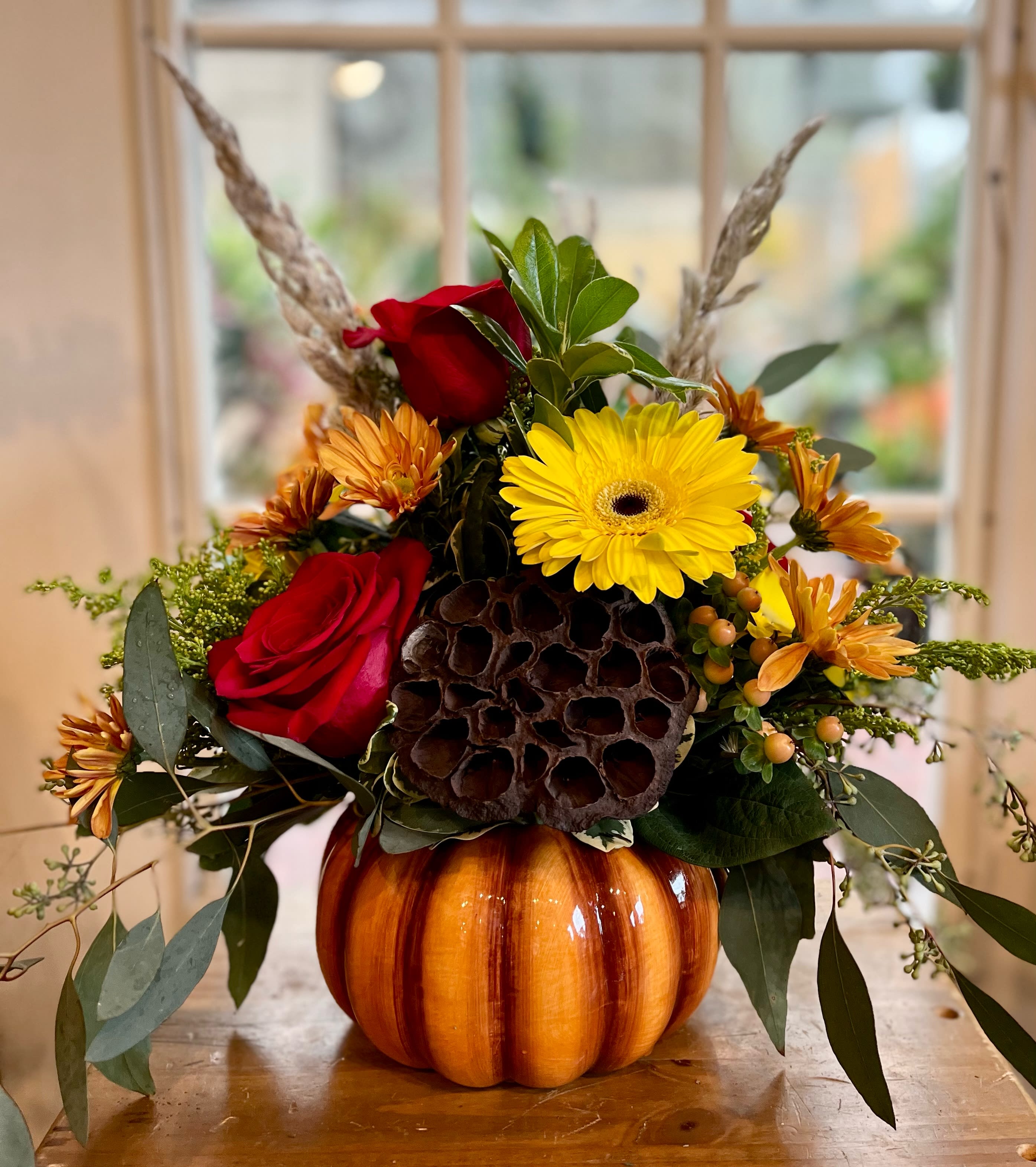 Autumn floral arrangement in a pumpkin container with red roses and yellow daisies
