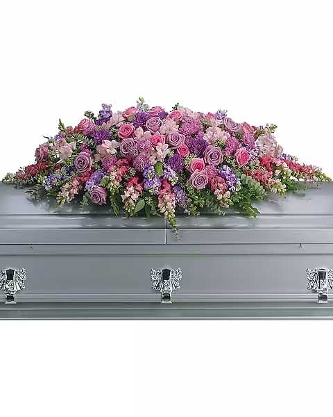 Lavender Tribute Casket Spray - Like a heartfelt embrace, this beautiful casket spray delivers comfort and love in an extraordinary way. A wonderful array of lavender and pink flowers with just the right amount of greenery is a lovely way to pay tribute to someone who will always be with you in heart, mind and spirit. Lovely lavender and pink roses, snapdragons, alstroemeria, chrysanthemums, fern, eucalyptus and more create this tribute that is overflowing with grace and love. 