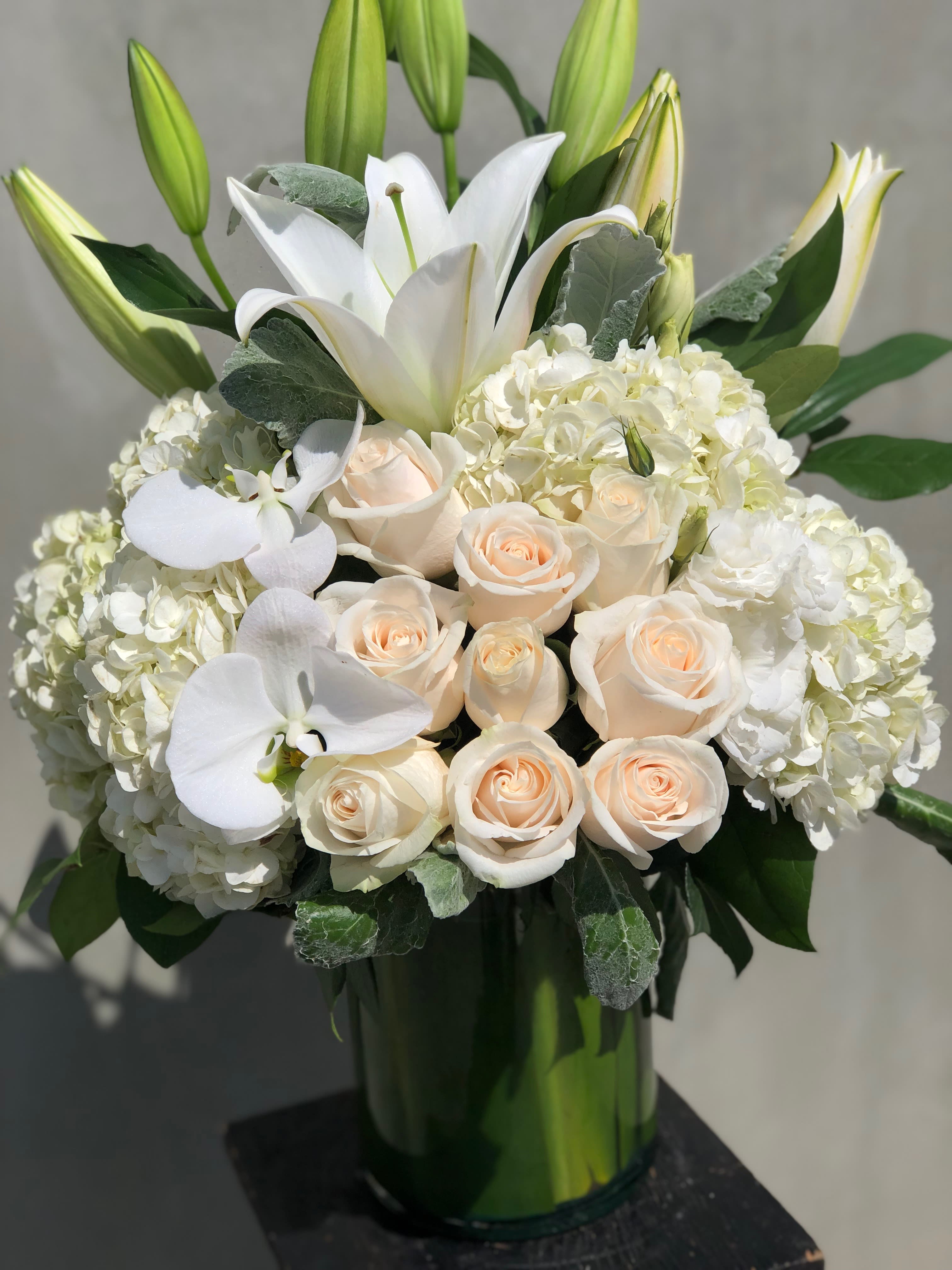 White lilies and pale roses arranged in a tall glass vase