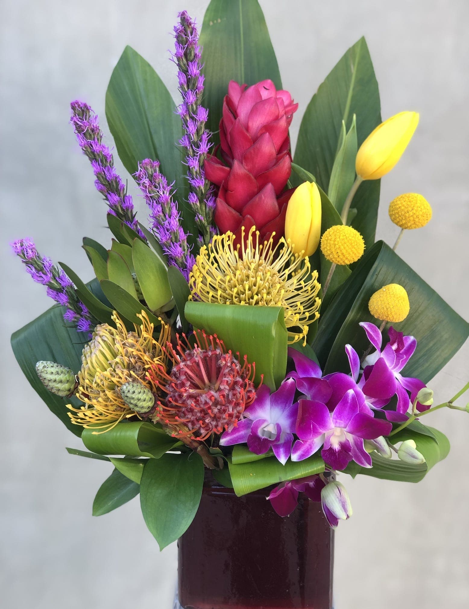 Tropical bouquet with orchids, pincushion protea, and yellow tulips in a vase