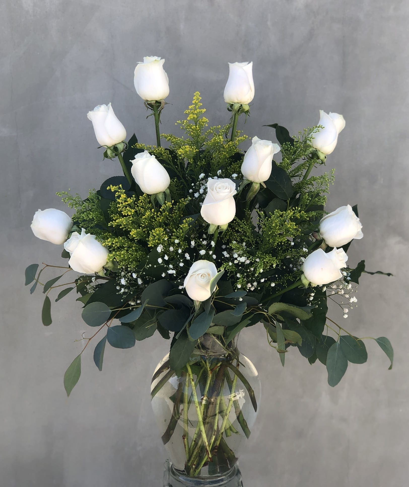 White roses arranged in a clear glass vase with green foliage.