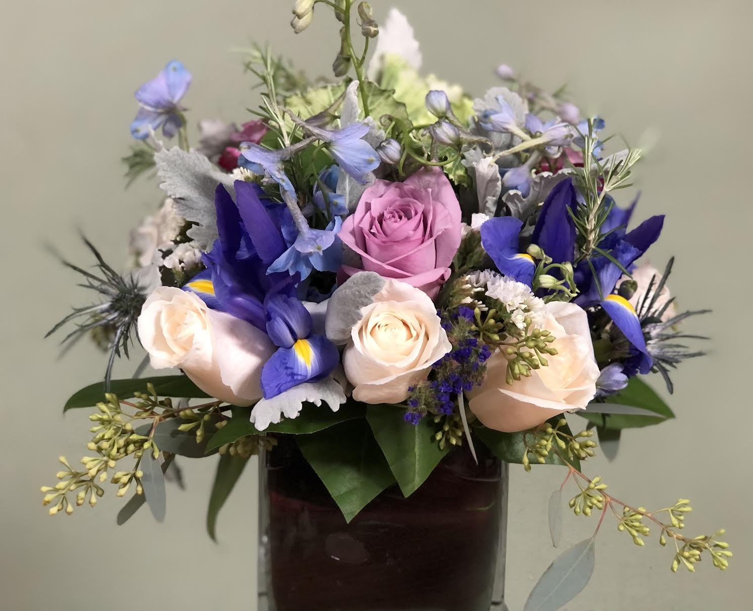 Mixed bouquet of roses and blue flowers in a glass vase