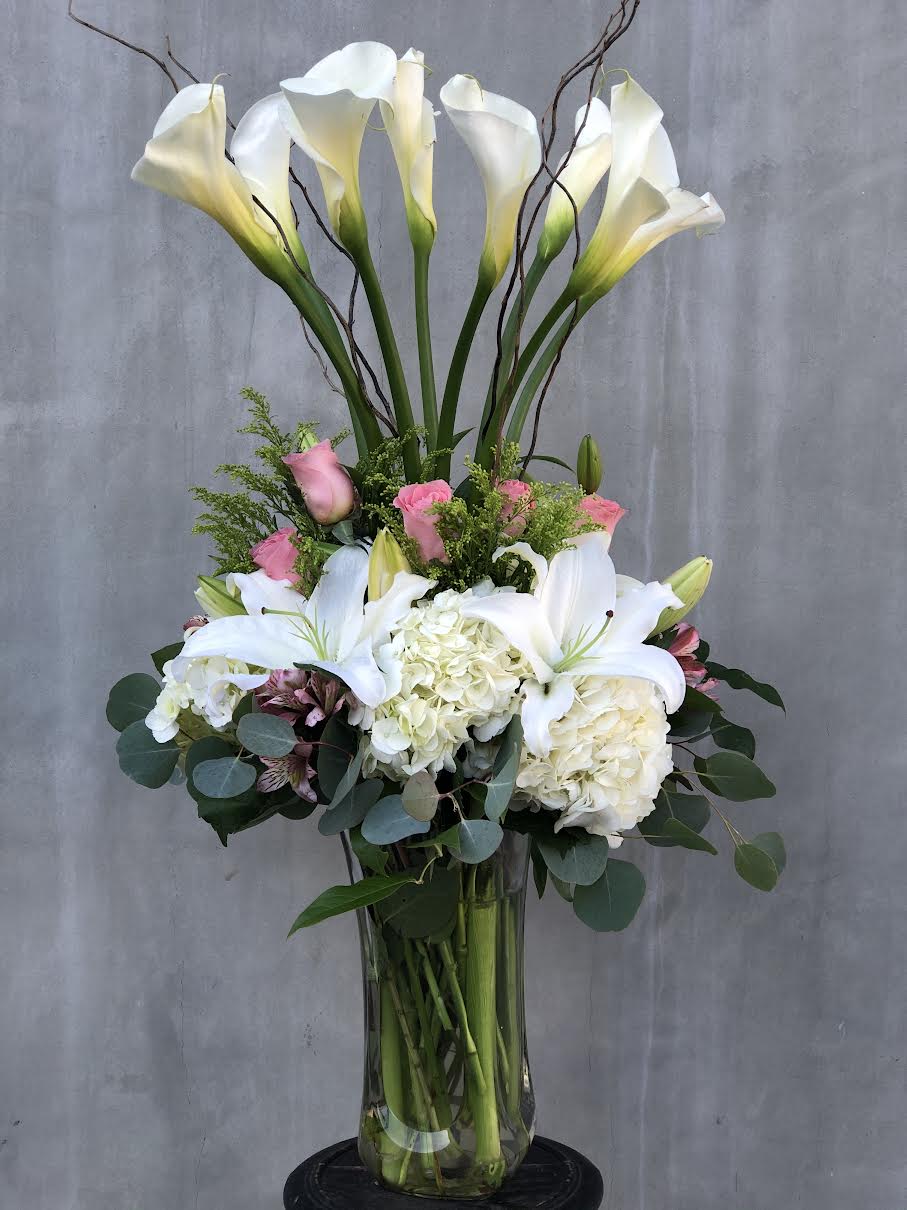 Tall bouquet of white calla lilies, pink roses, and white hydrangeas in a glass vase