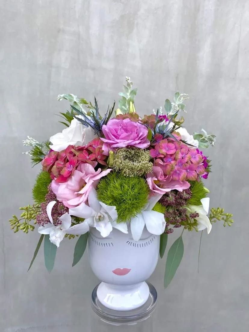Pink and white floral arrangement in a white face vase