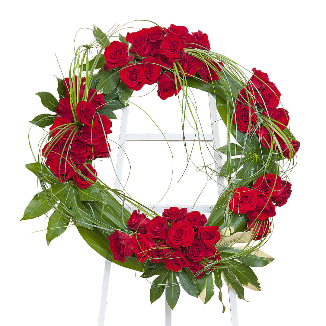 Red rose wreath with green foliage on a white stand