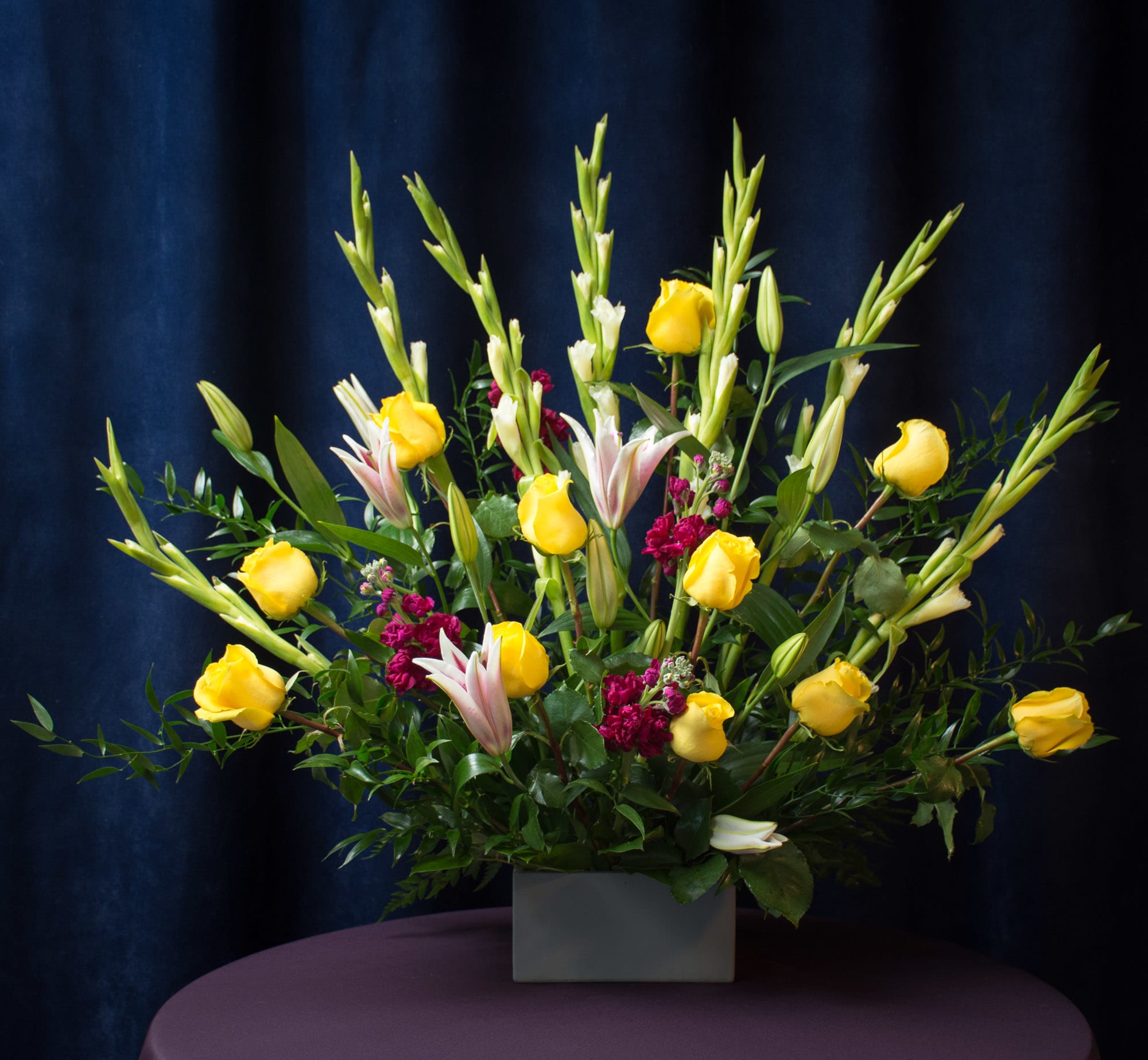 Yellow roses and lilies arranged in a square vase