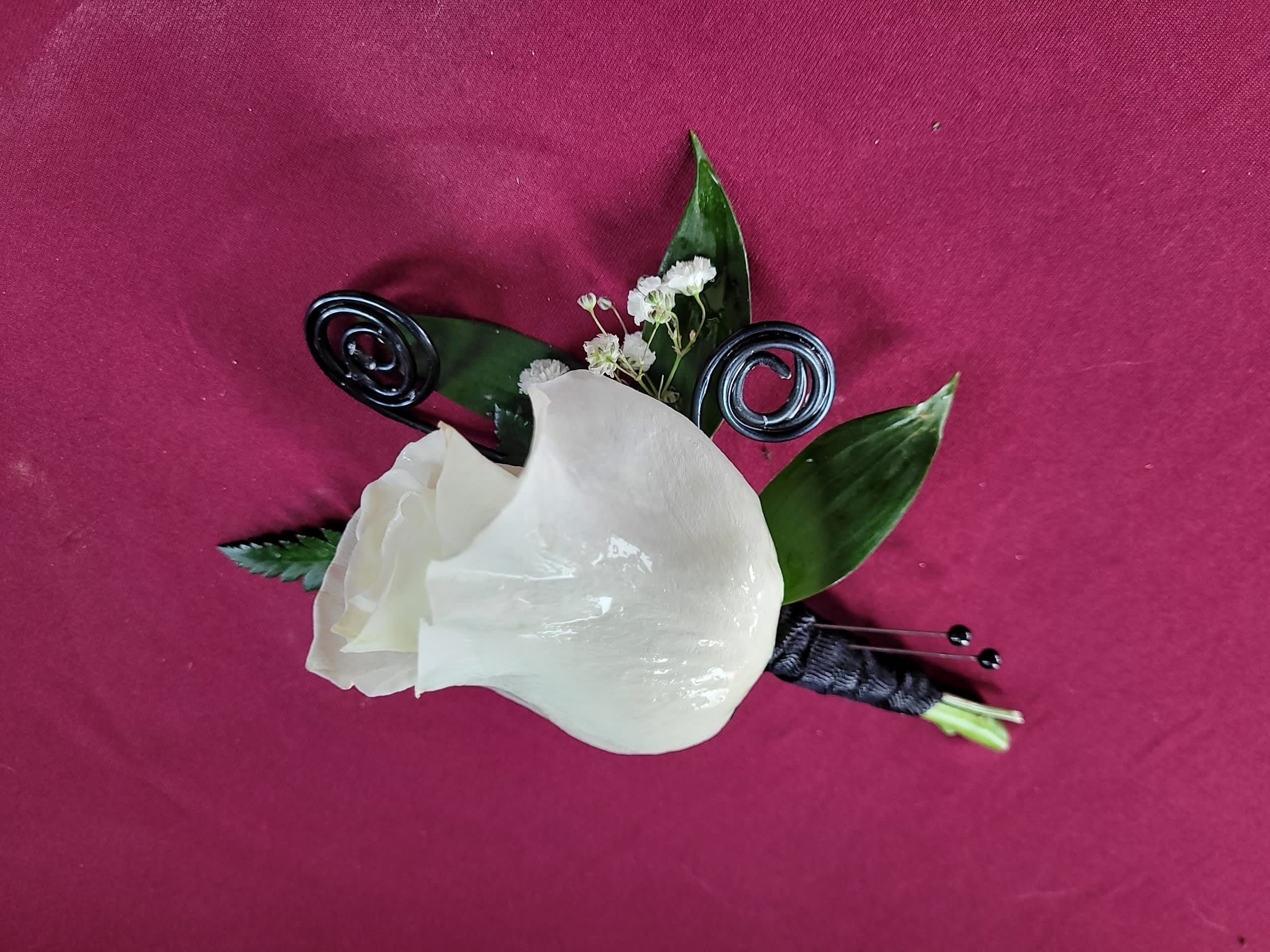 White calla lily boutonniere with dark green leaves on a magenta background