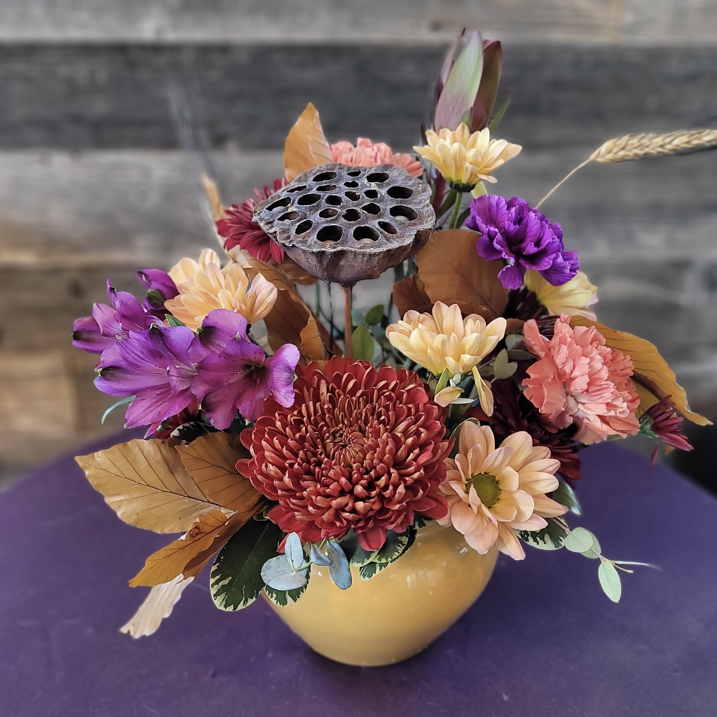 Mixed chrysanthemum arrangement in a yellow vase with dried lotus pod