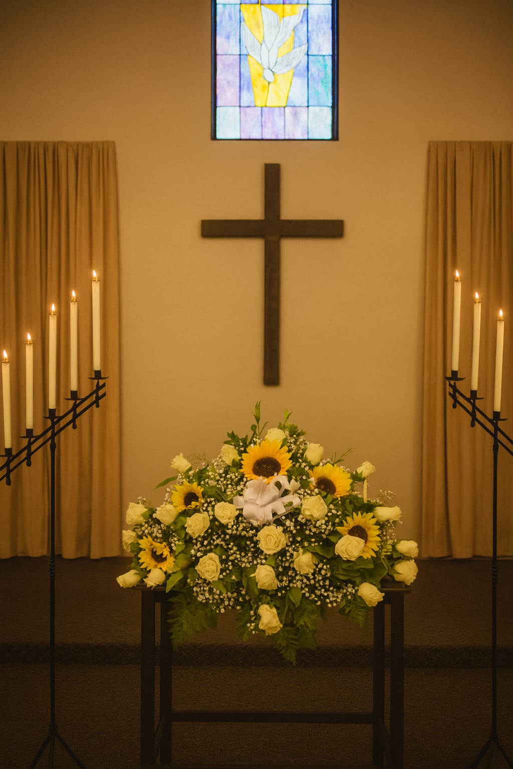 White rose and sunflower funeral arrangement in a church with candles and a cross