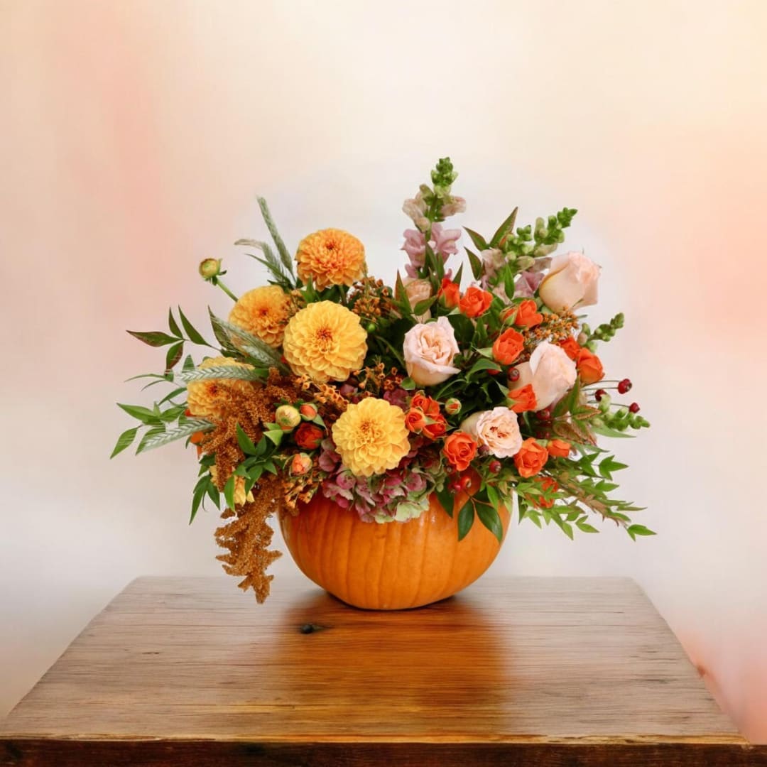 Floral arrangement in a pumpkin-shaped container with orange and peach blooms