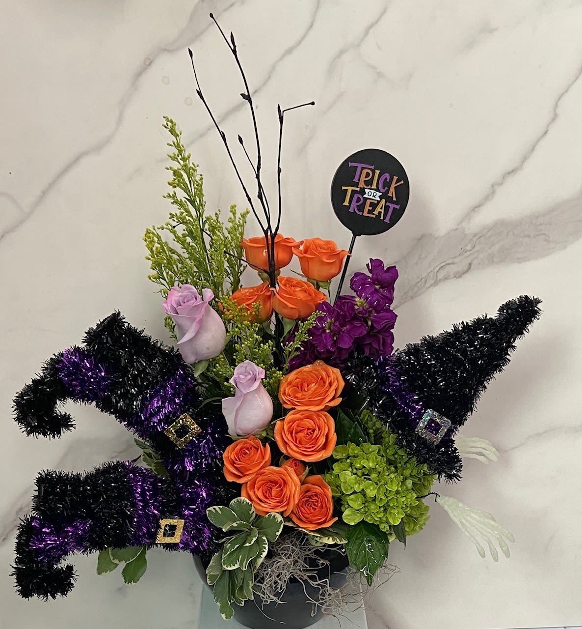 Halloween arrangement with orange and purple roses in a black container