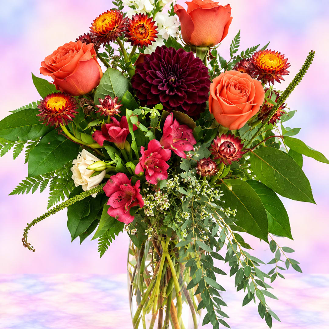 Bouquet of orange roses, burgundy dahlias, and pink lilies in a glass vase