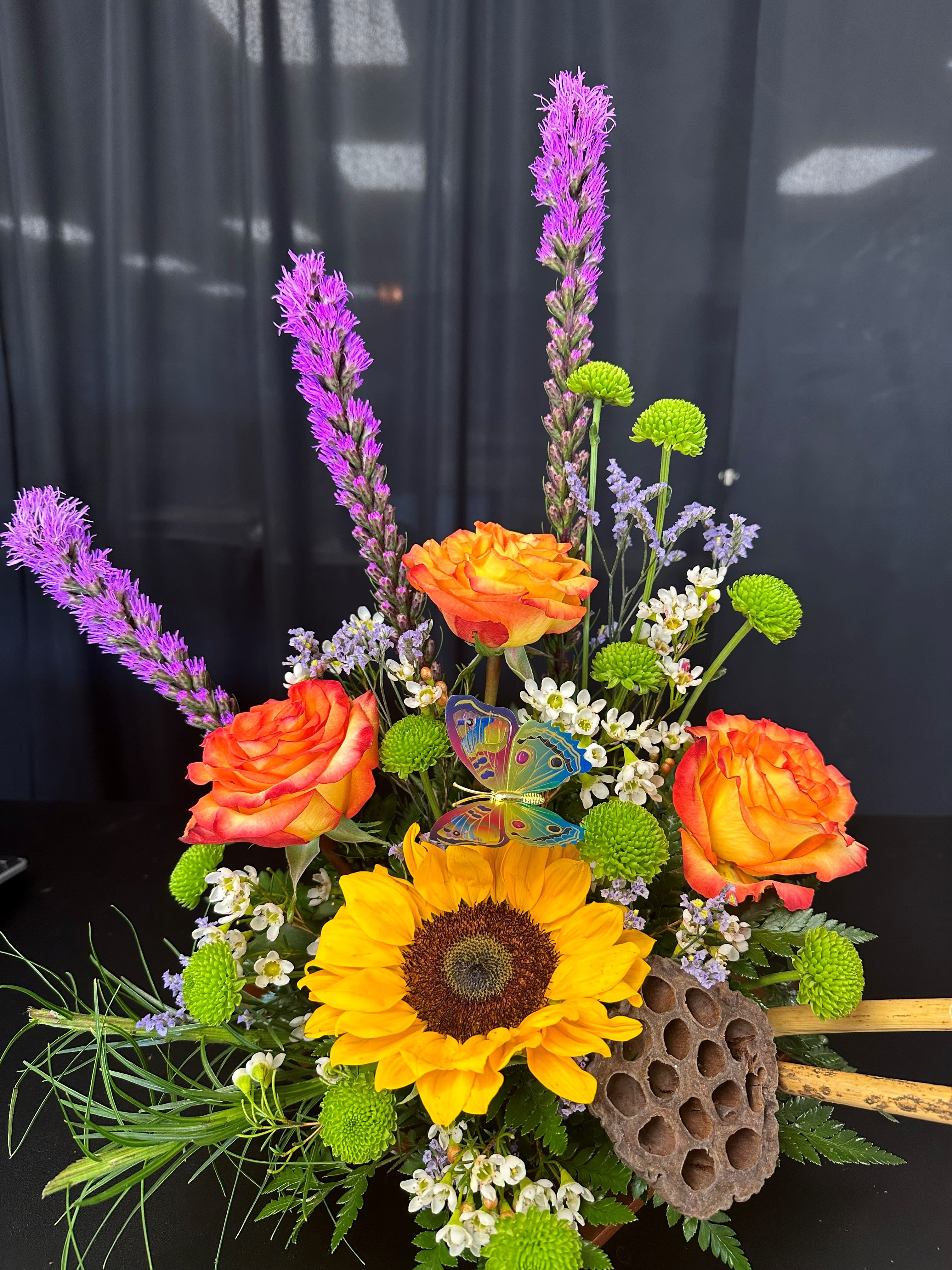 Bouquet with orange roses, a sunflower, and purple spikes in a decorative vase